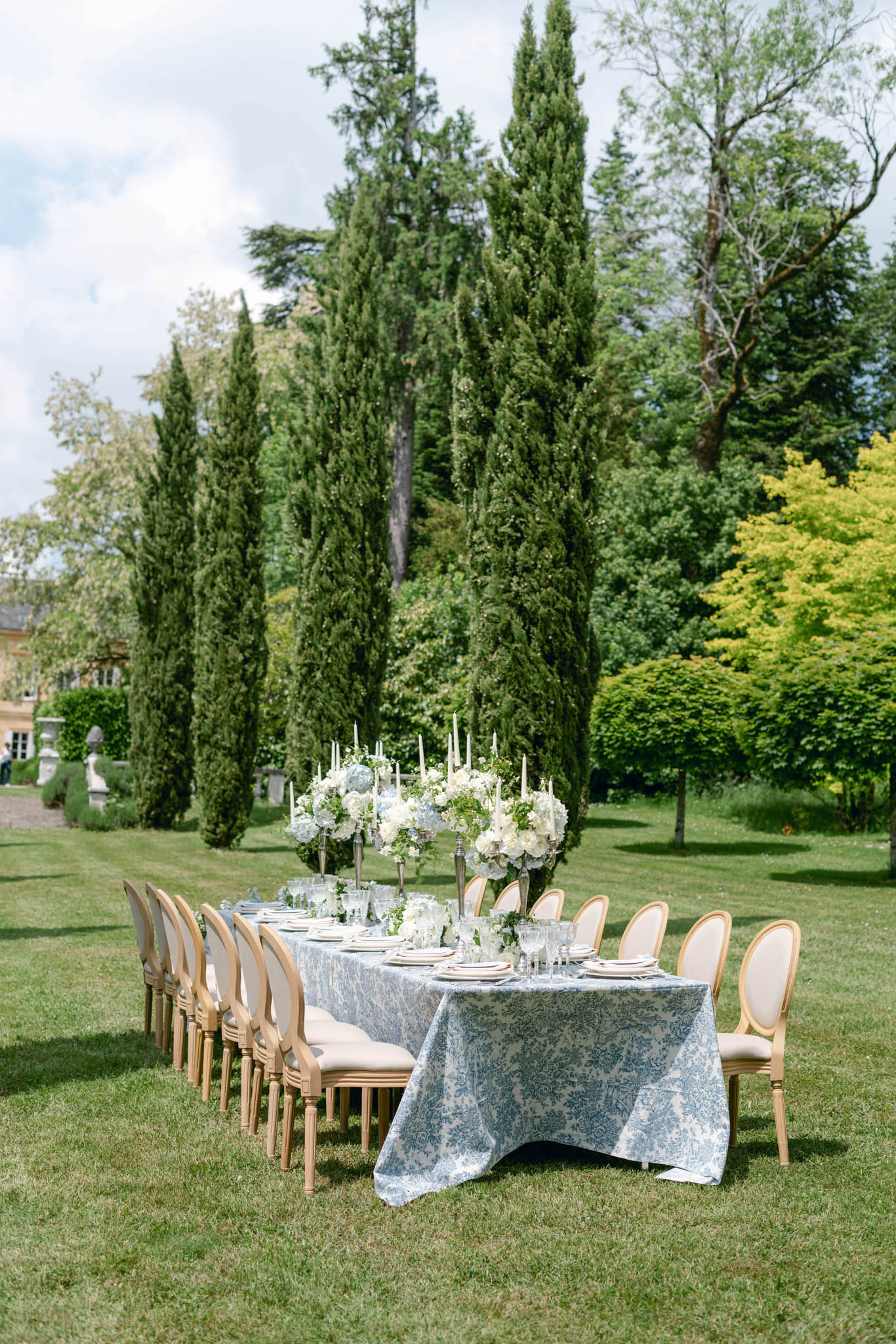 Long table in blue damask linen with white and blue hydrangea compotes and silver candelabras on lawn
