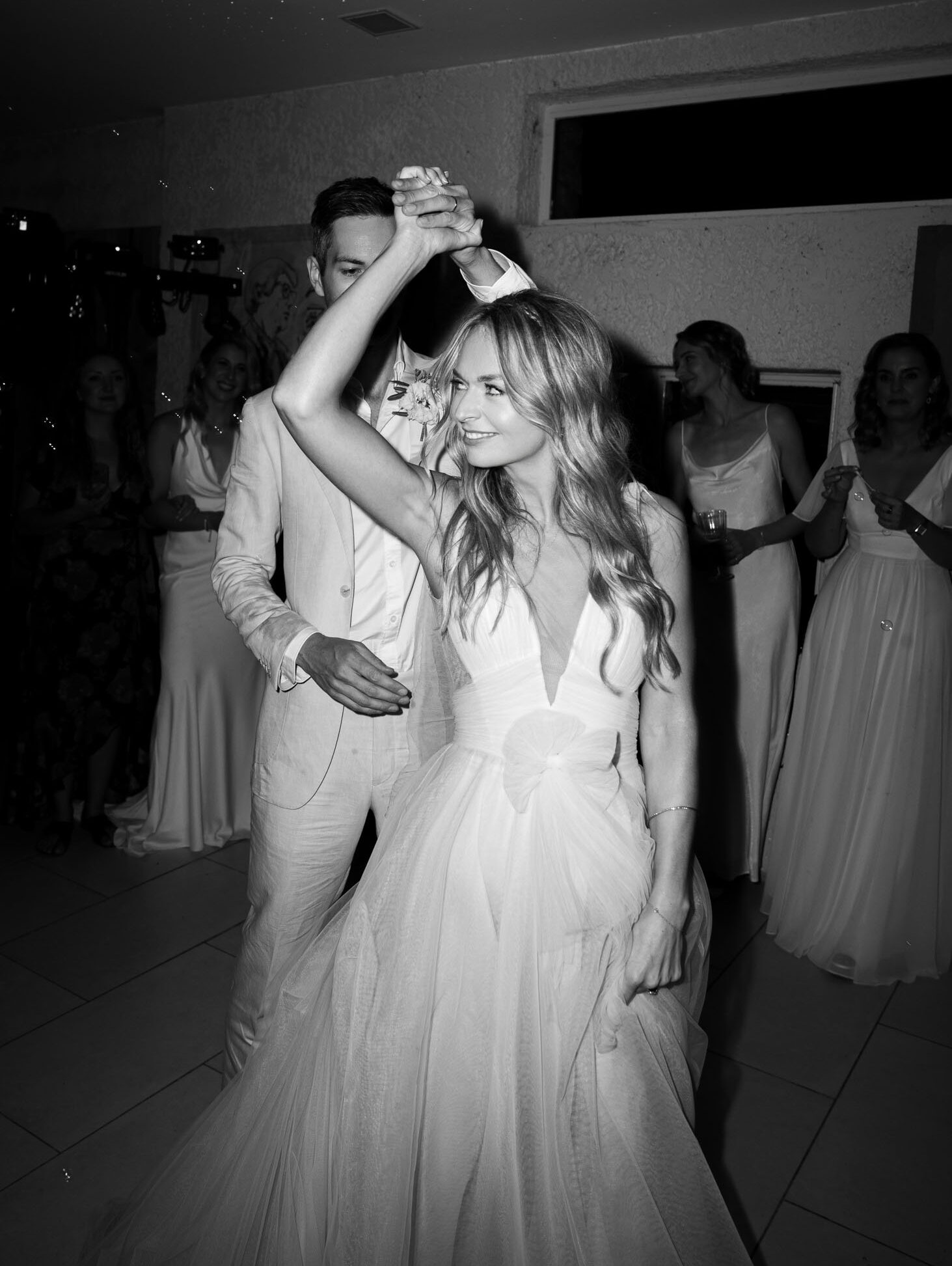 Black-and-white photo of couple's first dance with groom spinning the bride in a tulle ballgown at an indoor reception