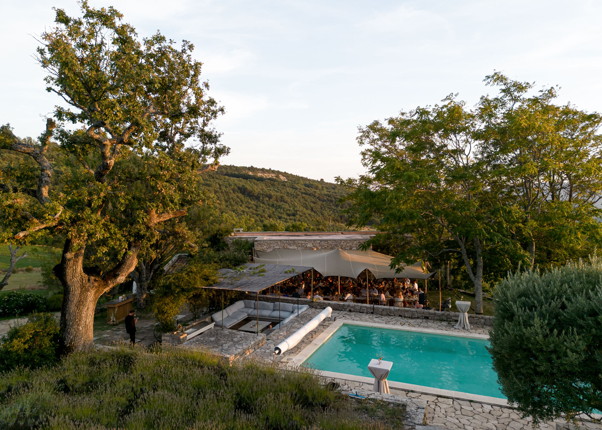 Aerial view of reception under sail-shade canopy beside pool and stone terrace at Provencal property