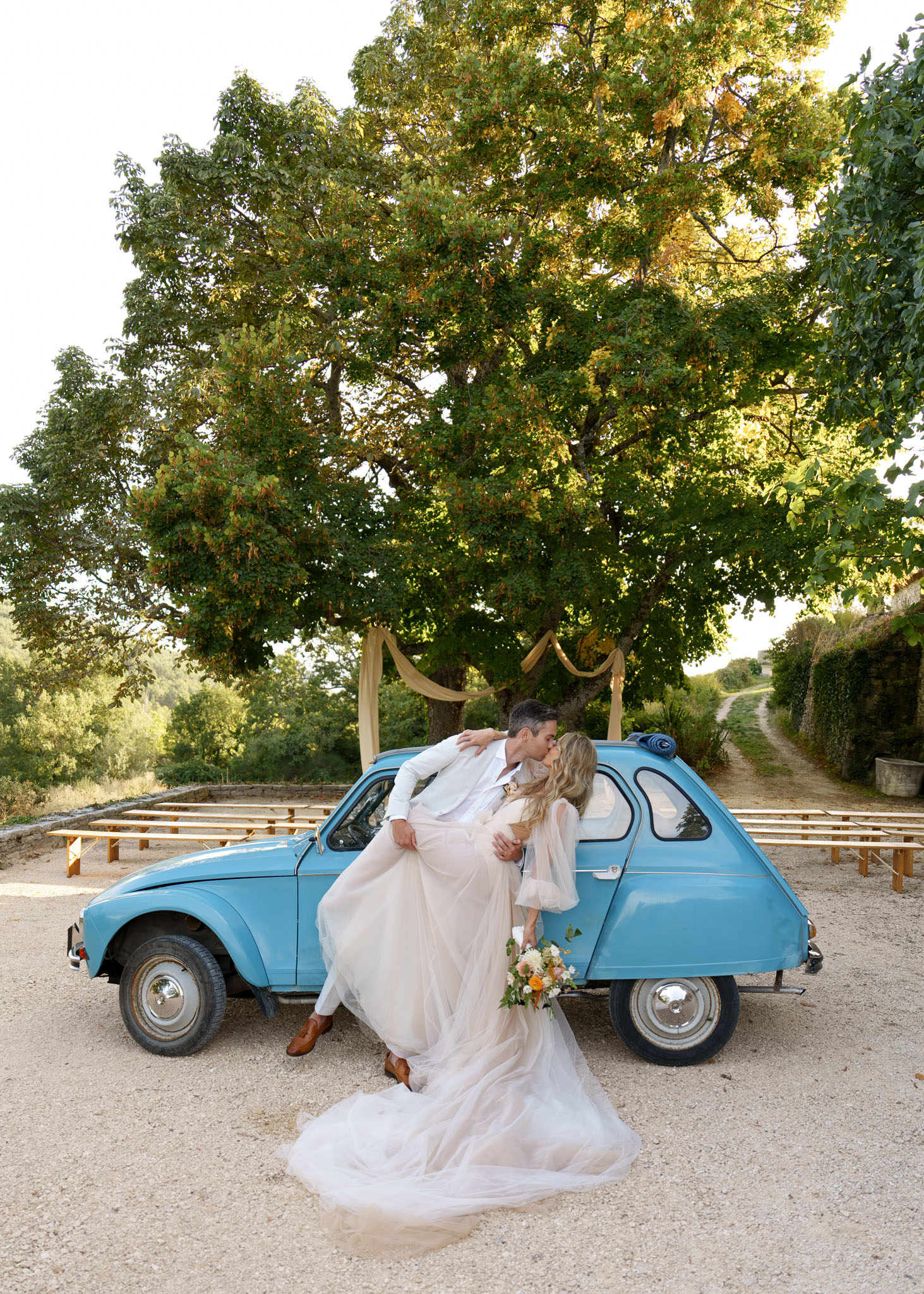 Couple dip-kissing before vintage blue Citroen 2CV with orange and yellow wildflower bouquet
