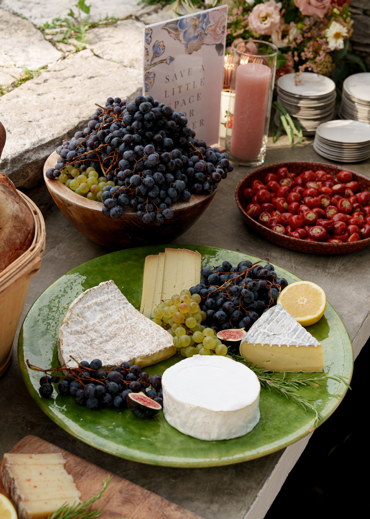French cheese board with camembert, grapes, figs, and rosemary on green ceramic platter at outdoor station