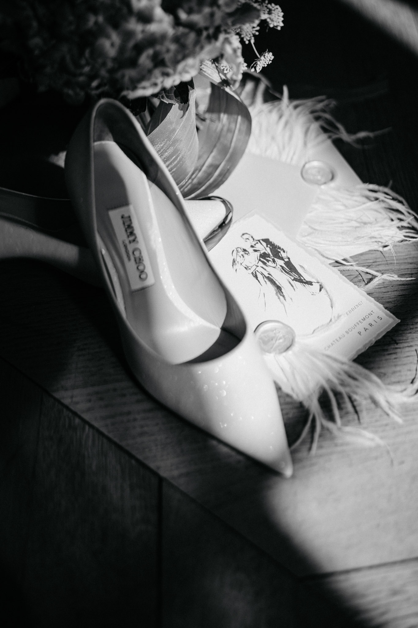 Jimmy Choo sparkle heels on feather-trimmed stationery card with wedding bands in B&W