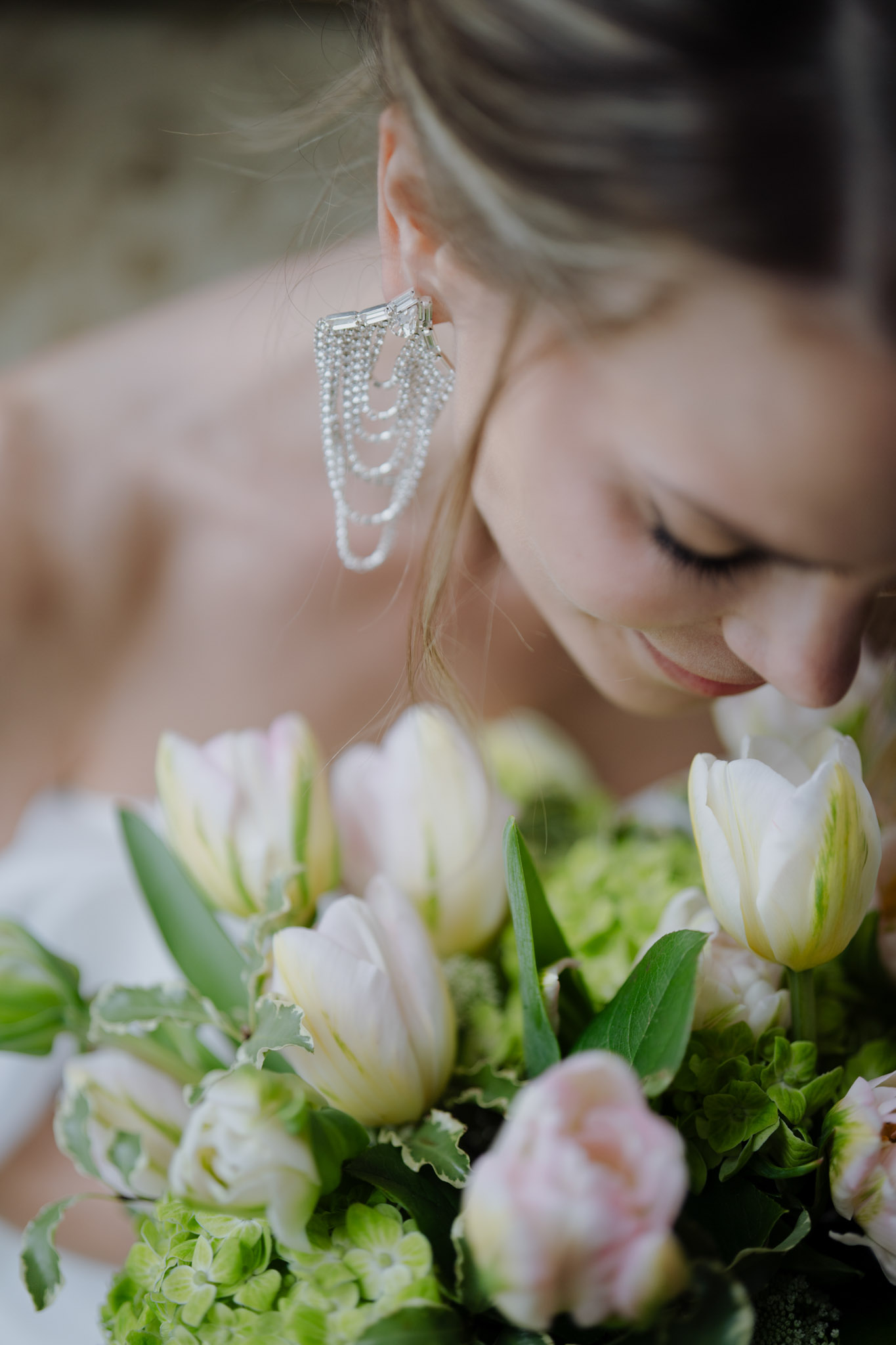 Close-up of bride with crystal chandelier earring looking down at bouquet of blush tulips and cream roses