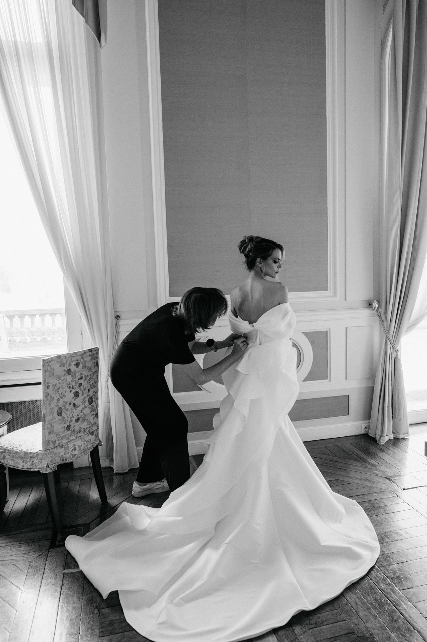 Black and white assistant fastening oversized bow-back ballgown in panelled chateau room with tall windows