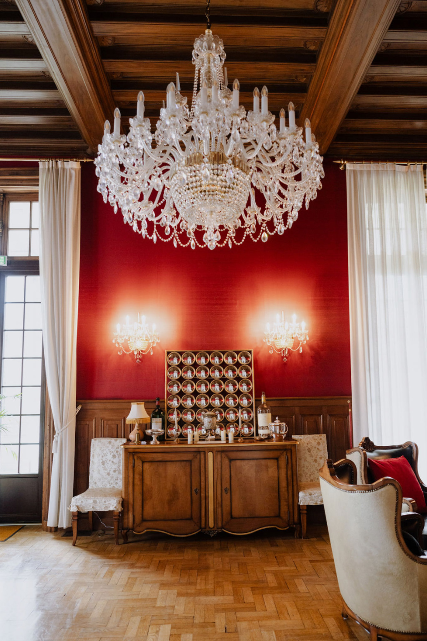 Crimson chateau salon with crystal chandelier parquet floor gold escort card display and white curtained windows