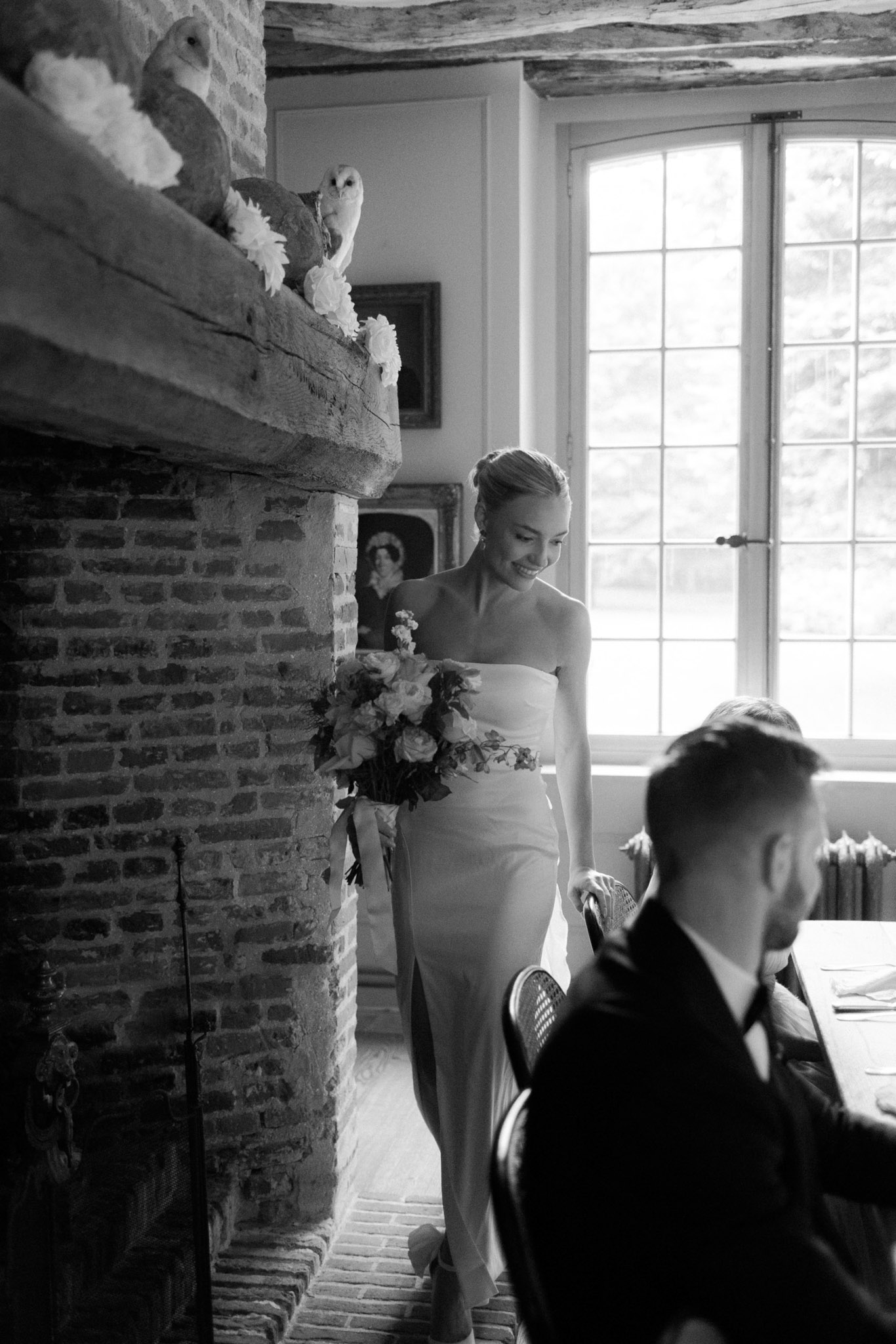 Bride walks toward groom at register table in stone-fireplace manor room during civil ceremony in B&W