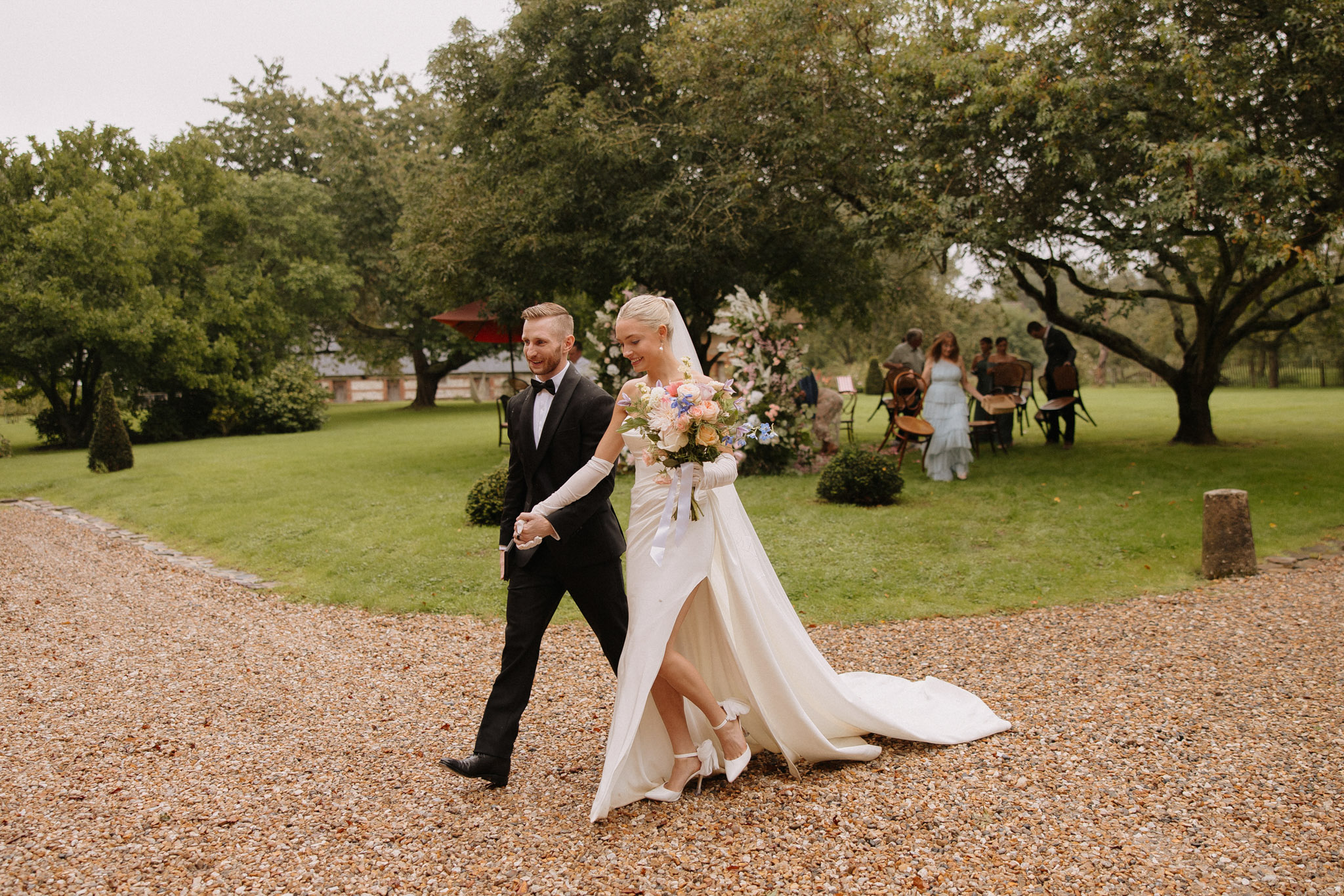 Couple walking from ceremony with peach and blue garden bouquet, cathedral train, and gloved bride