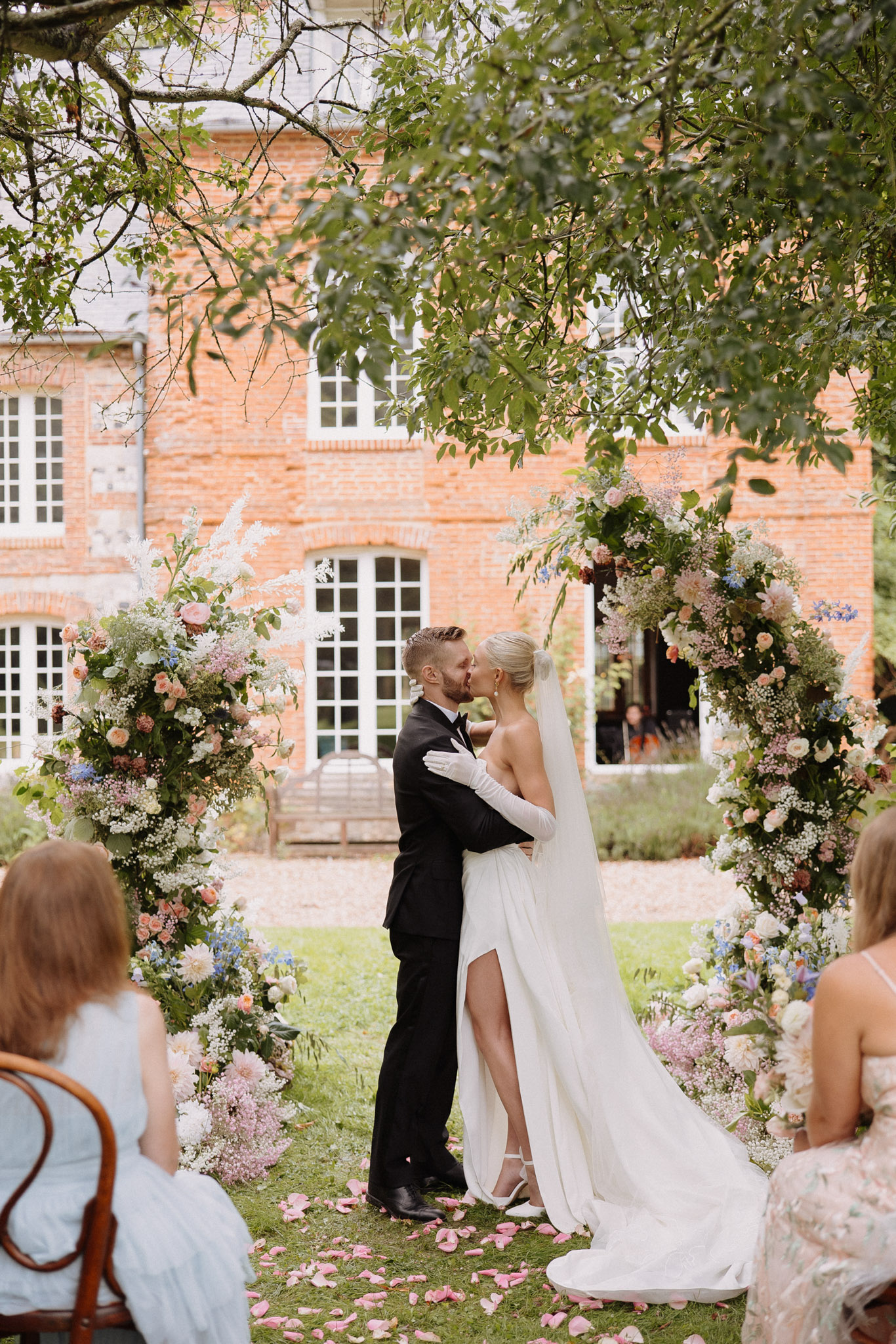 First kiss at red-brick manor with peach roses, lilac blooms, and blue delphinium columns