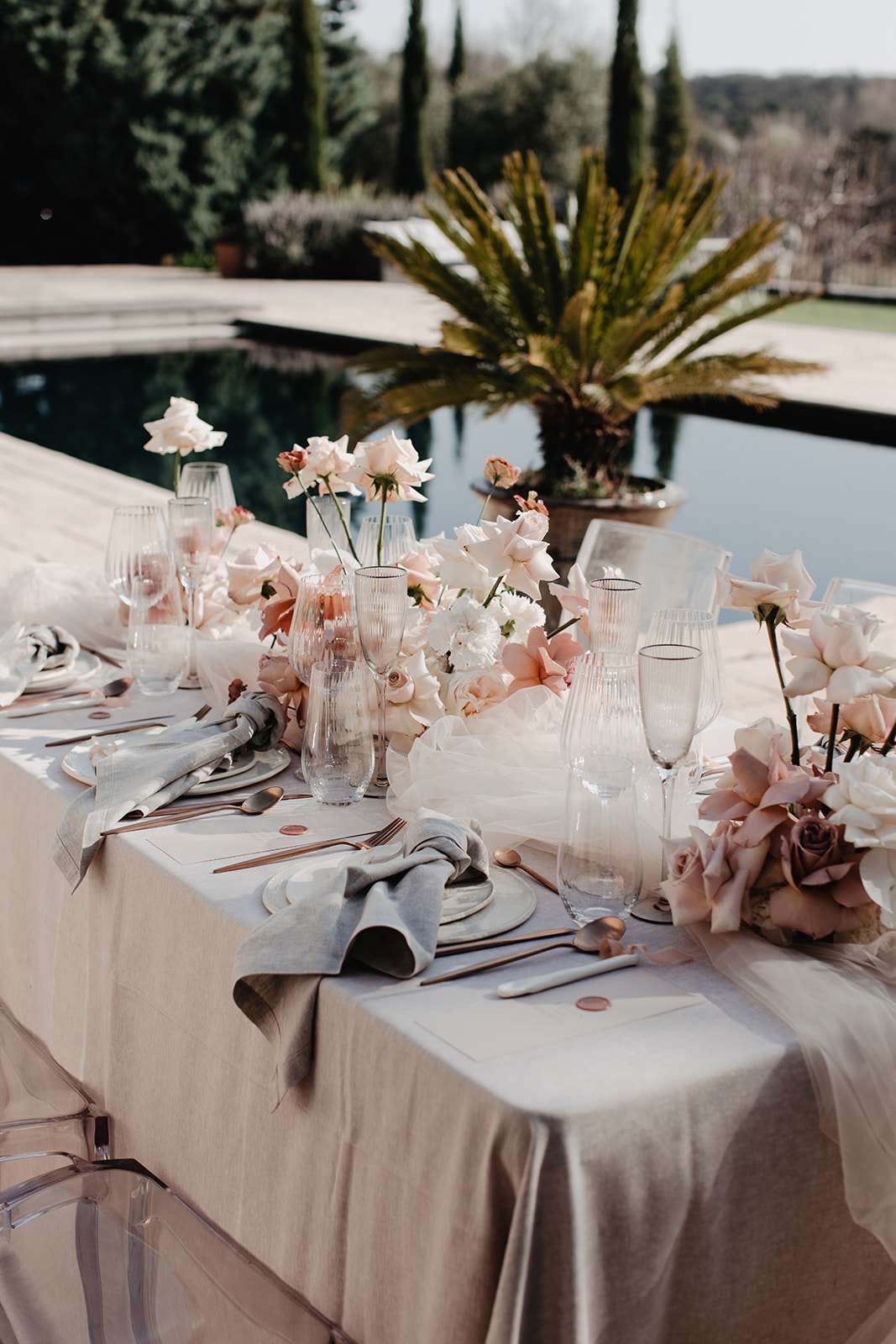 Reception table with blush and ivory rose runner, grey napkins, rose gold flatware, and terracotta wax-sealed envelopes by...