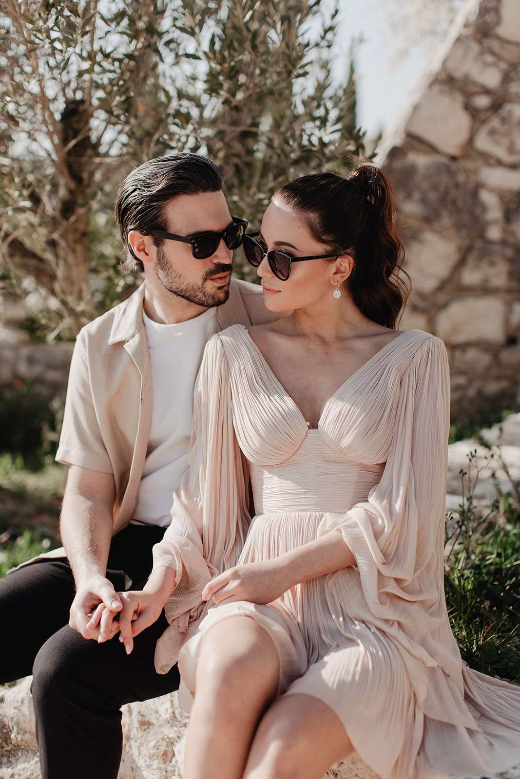 Couple seated together outdoors in coordinated warm neutral outfits with sunglasses in a South of France setting