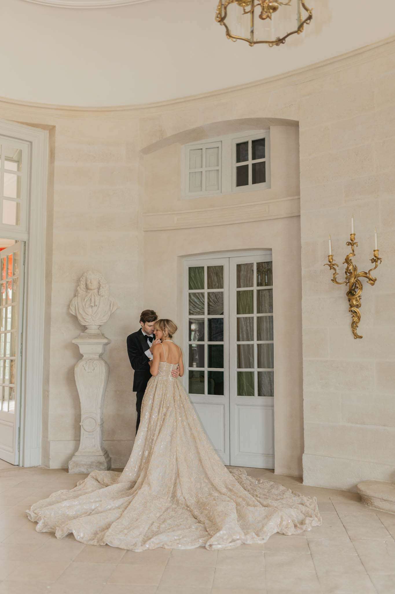 Couple stands in domed chateau salon, bride's champagne-gold ballgown train fanning across stone floor