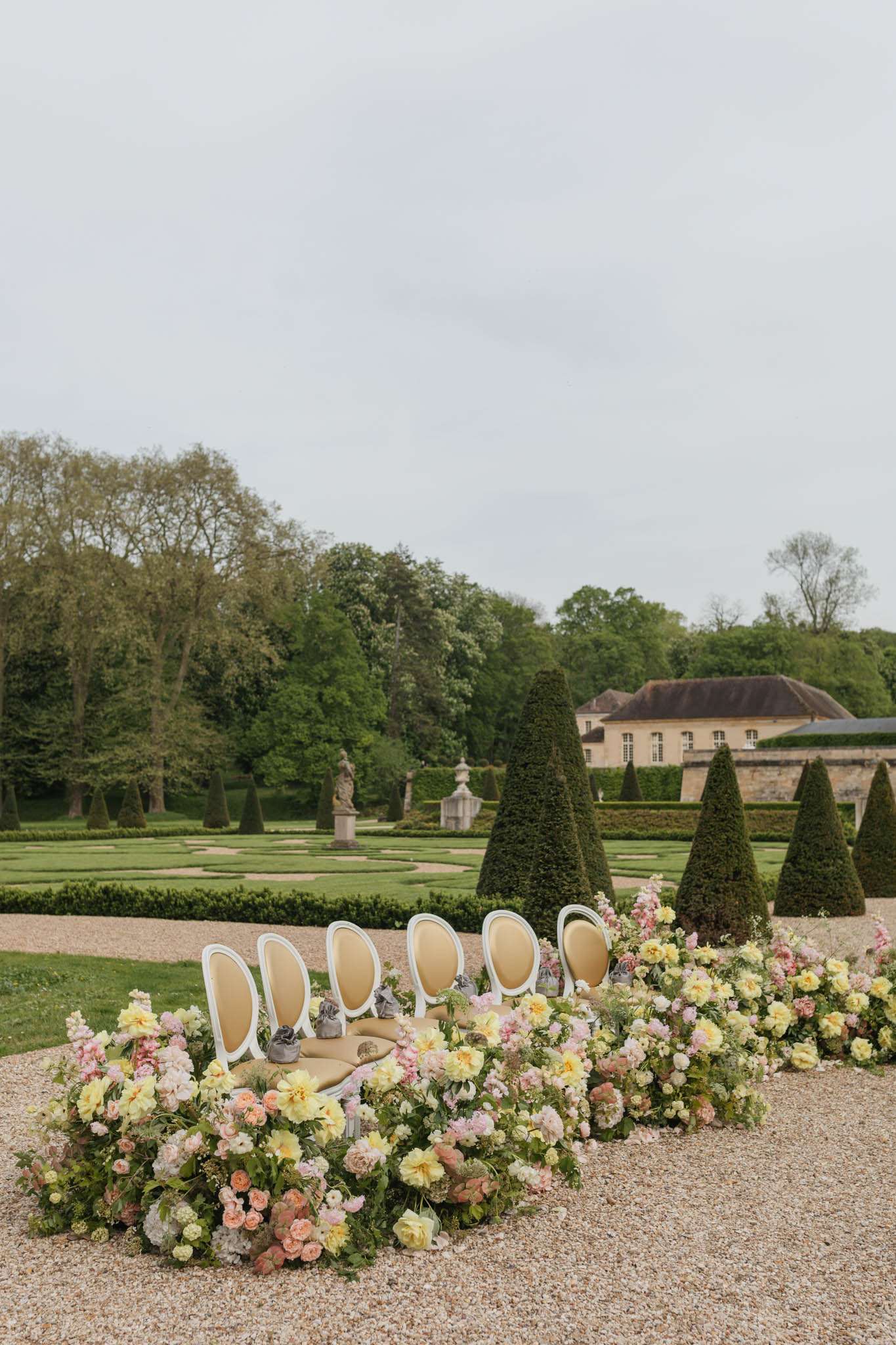 Ceremony chairs with pastel floral arrangements of dahlias and roses in a formal French chateau parterre garden
