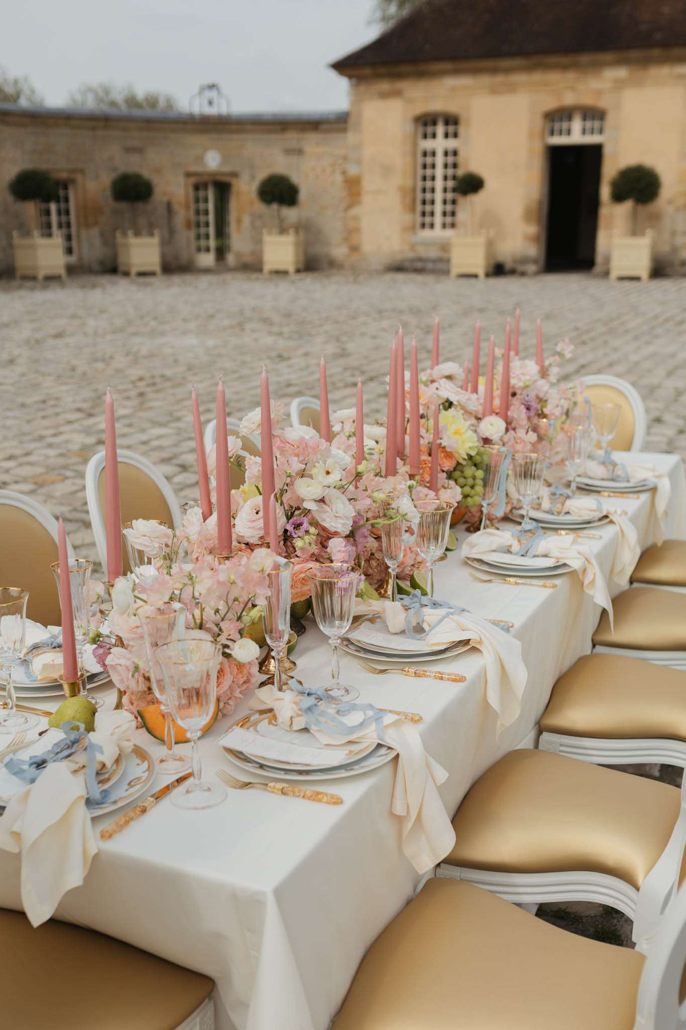 Louis XVI chairs at table with blush ranunculus runner, dusty rose tapers, and blue-patterned china on courtyard