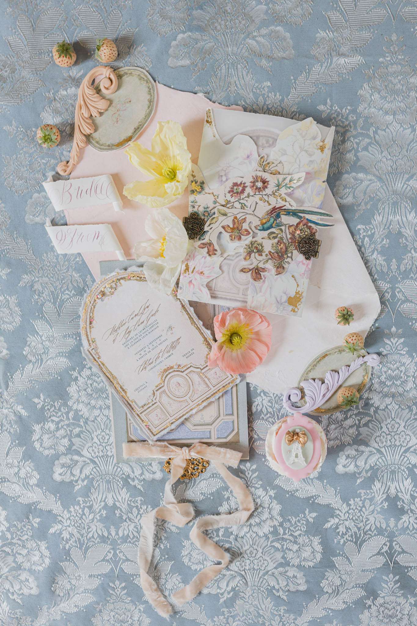Flat lay of wedding stationery suite with heart-shaped invitation, calligraphy cards, and velvet ribbon on blue damask