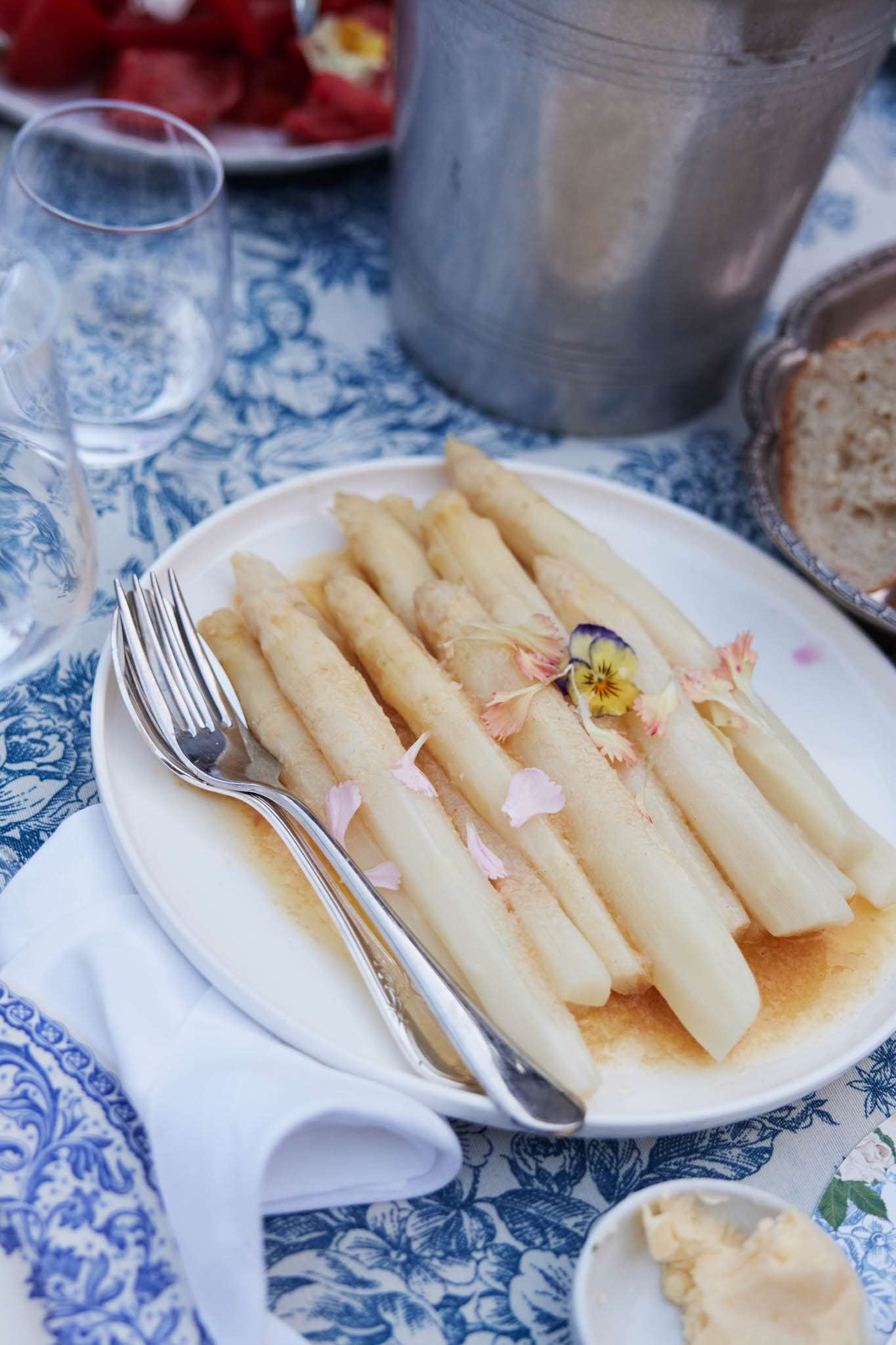 Plated white asparagus starter on blue and white toile tablecloth with silver champagne bucket