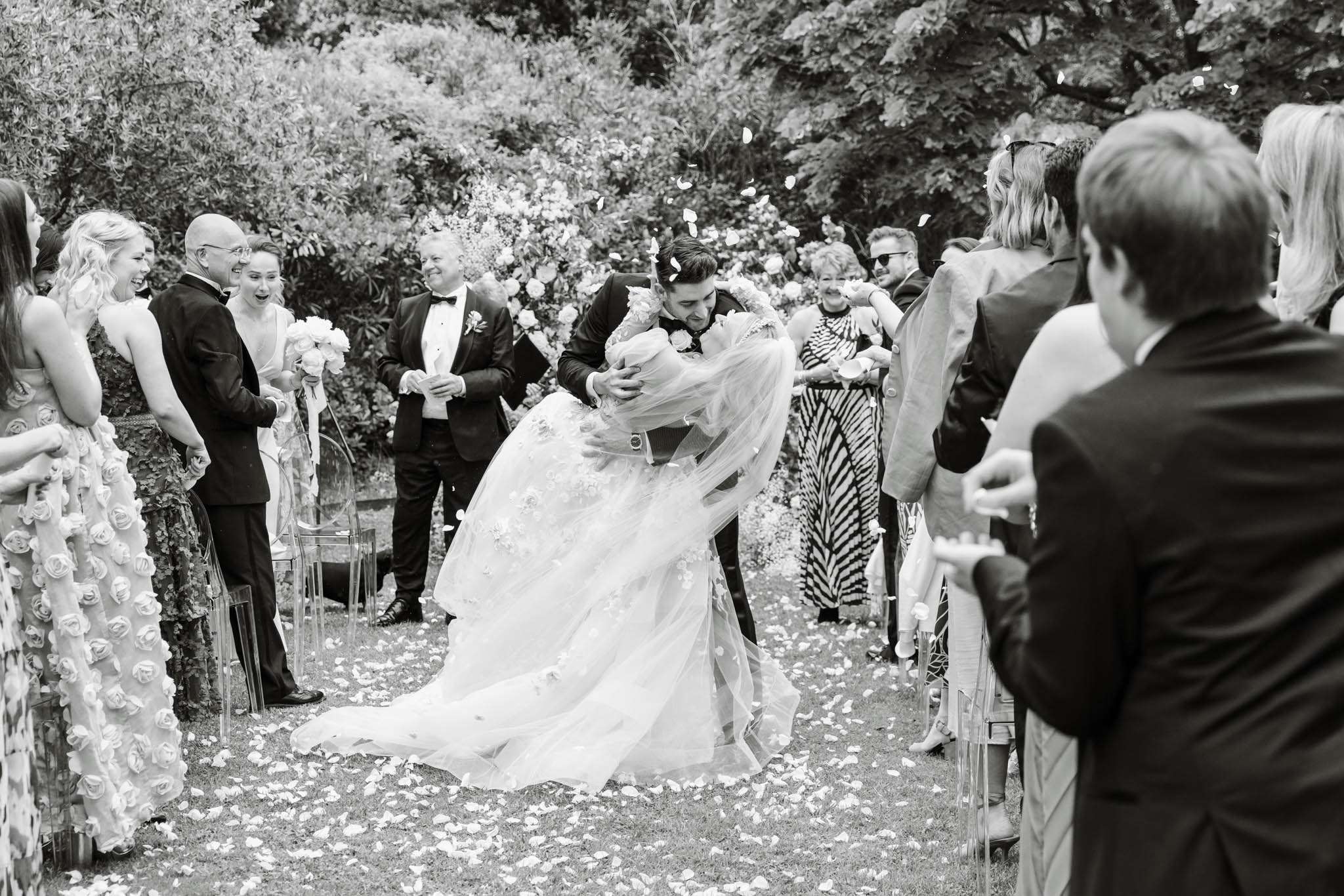 Black and white dip kiss with petal toss past ghost chairs, bride in floral applique ballgown and veil