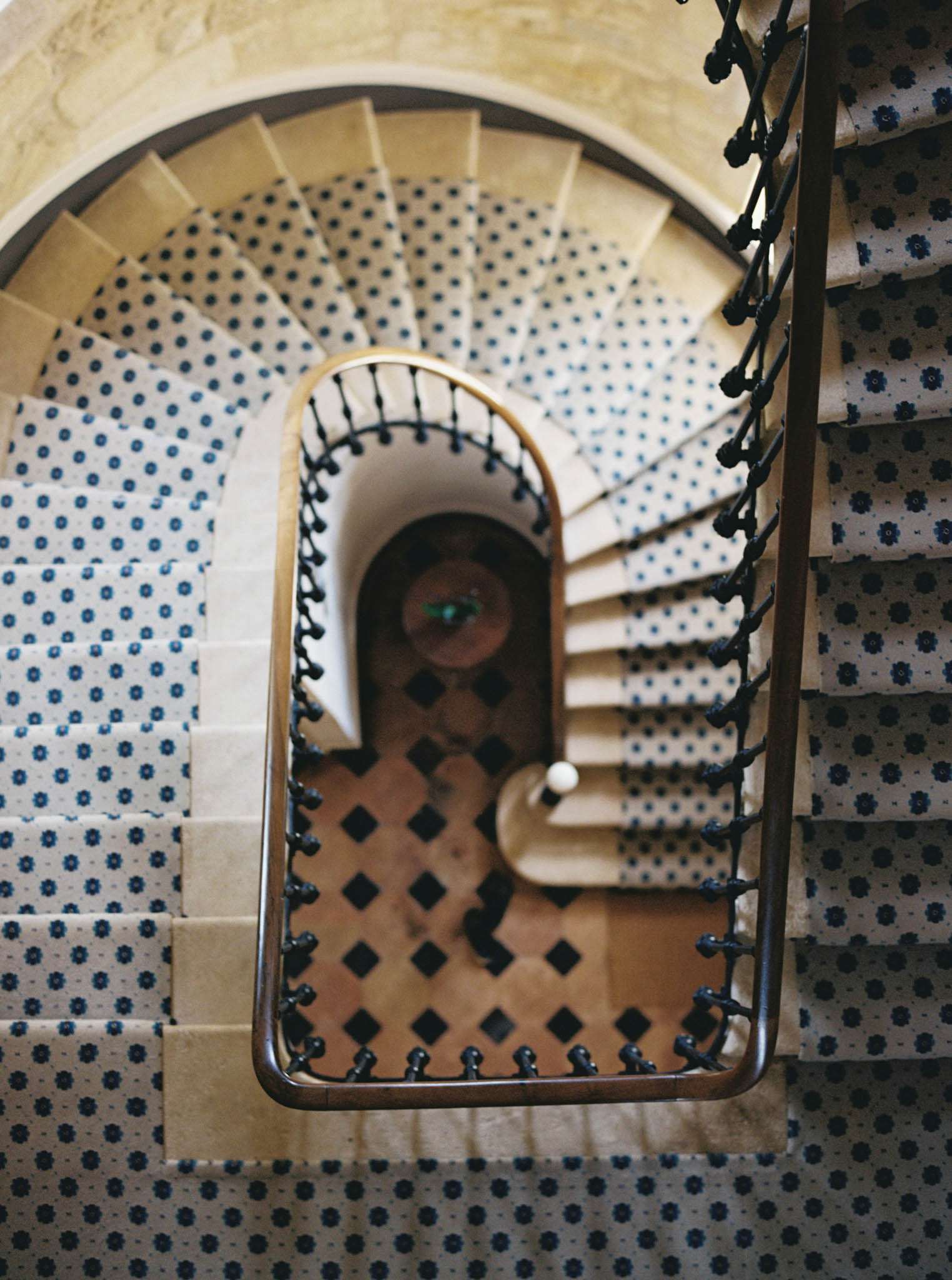 Top-down view of spiral stone staircase with navy patterned runner and wrought iron handrail in chateau
