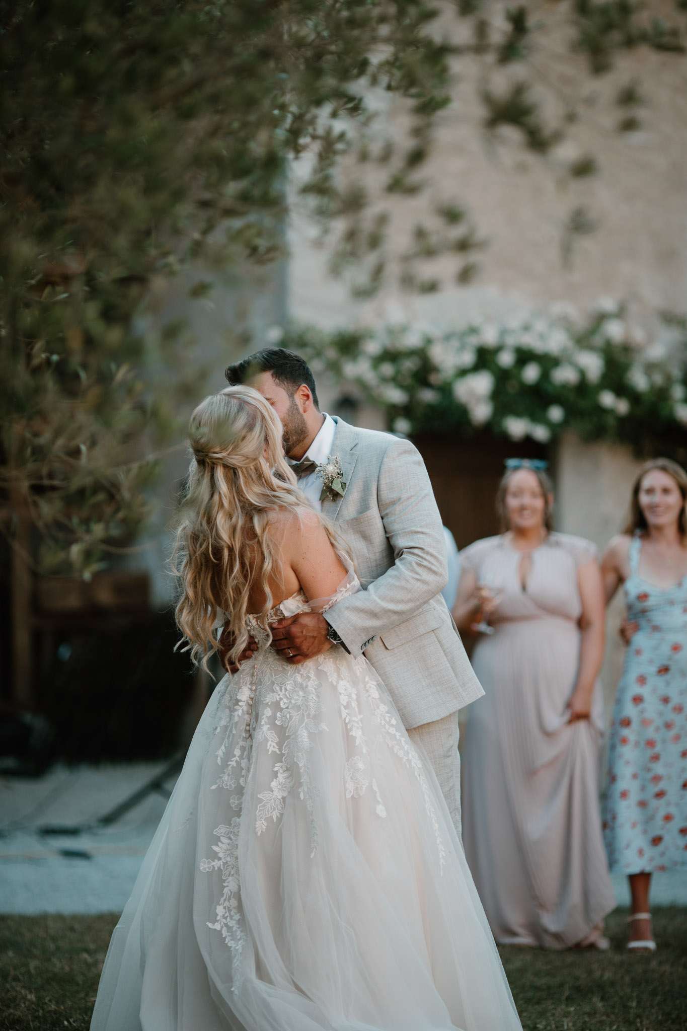 Couple sharing kiss during first dance outdoors with climbing roses and stone building behind