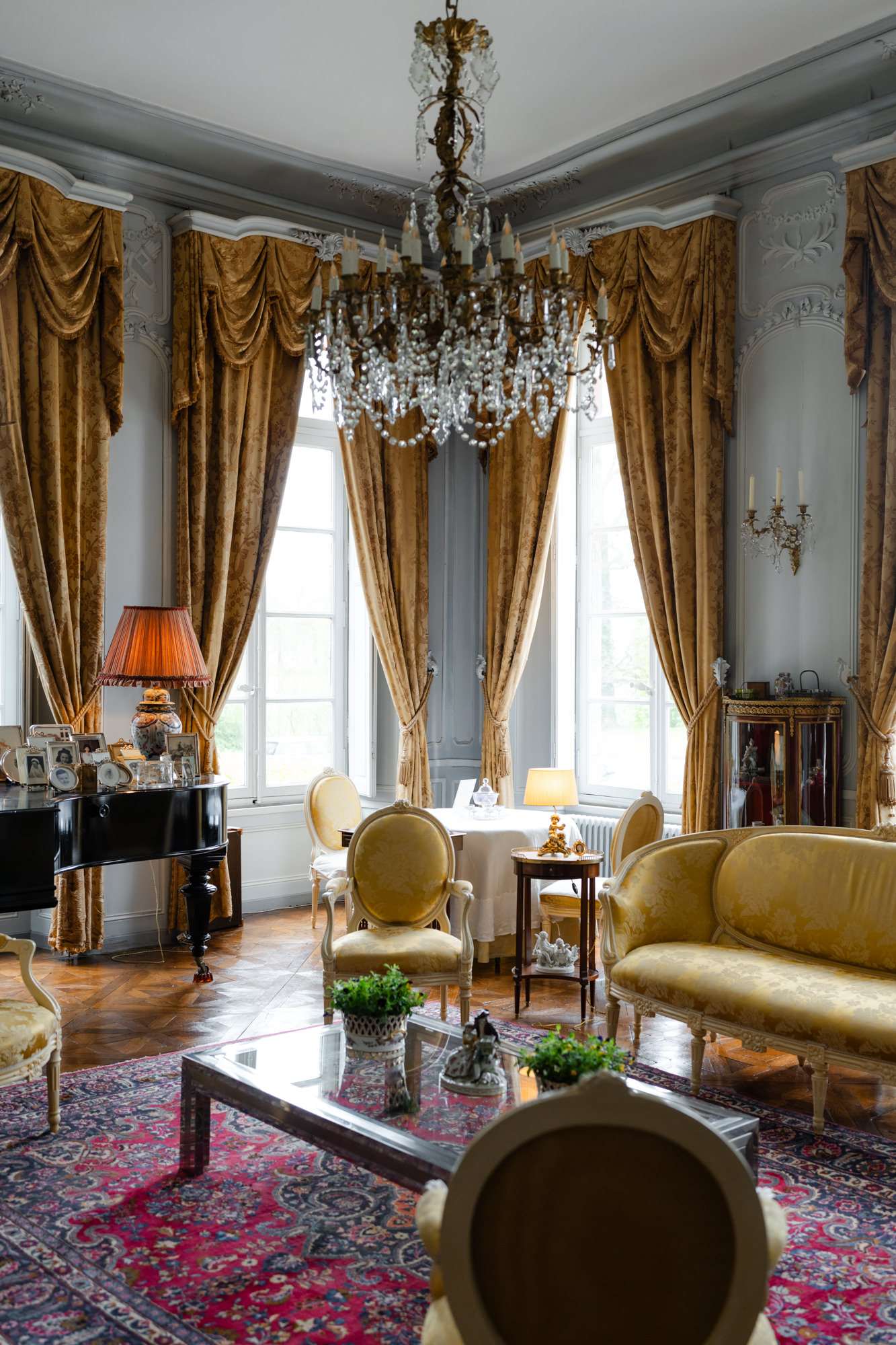 Classical salon with pale blue plasterwork walls, gold velvet curtains, Louis XVI chairs, and grand piano