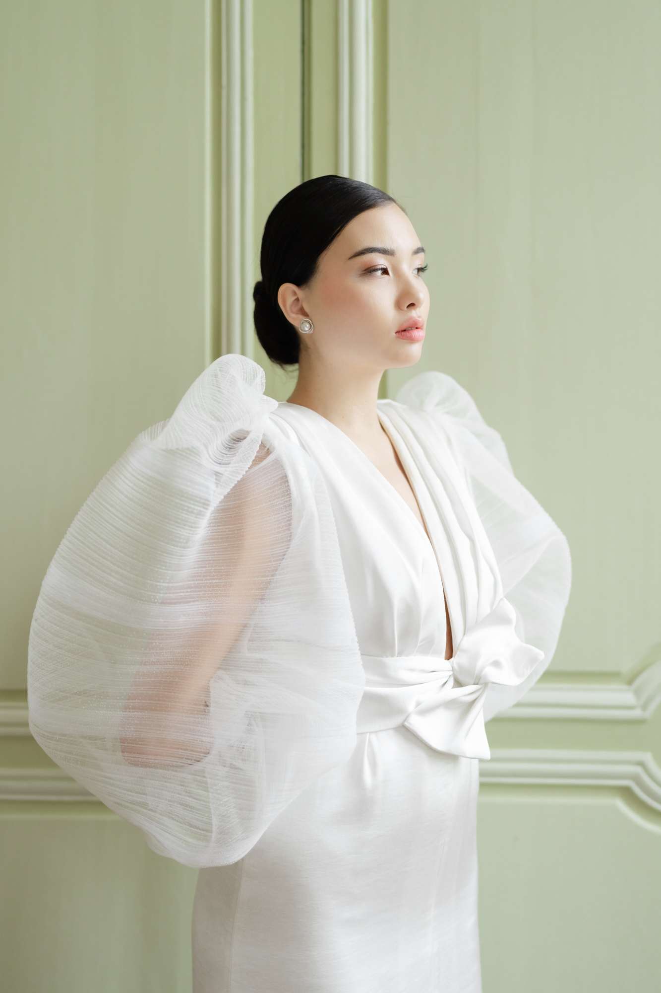 Bride in modern ivory dress with dramatic white cape against sage green wall