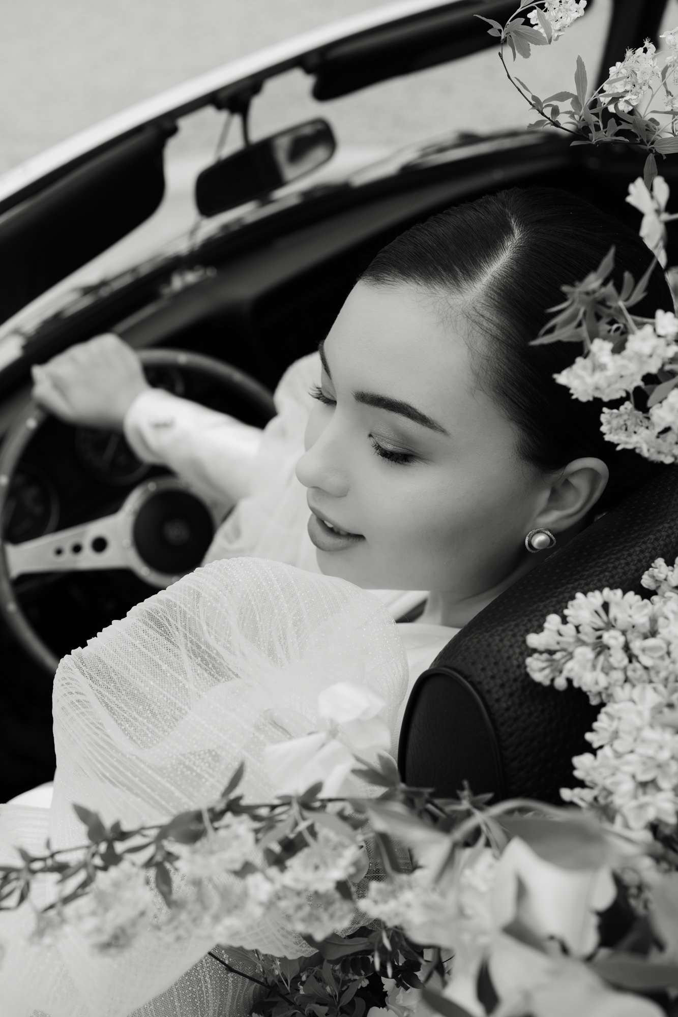 Black-and-white bride portrait in convertible car profile with white clustered bouquet in foreground