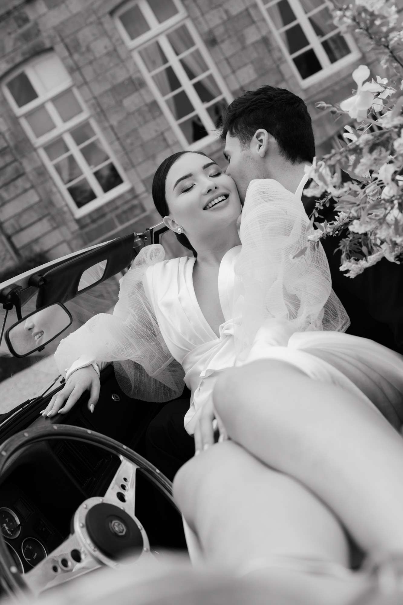 Bride and groom seated in convertible car, black and white, bride in white dress with white floral car decoration