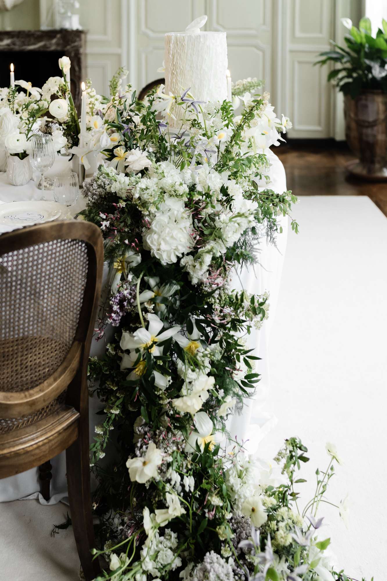 Reception floral garland with ivory dahlias, white daisies, and dusty purple astilbe beside white wedding cake