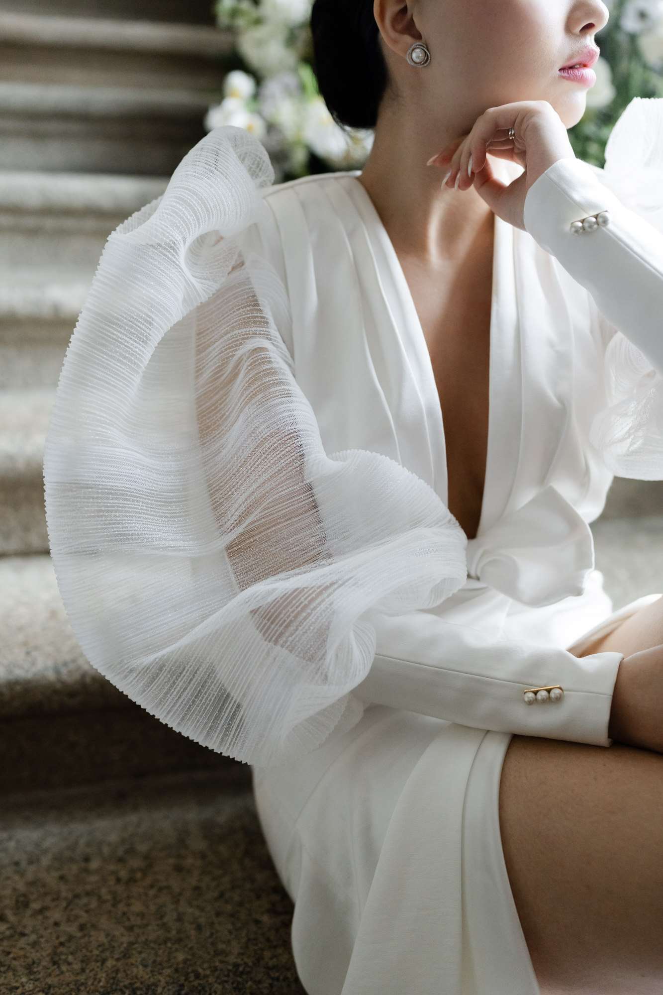 Bride in ivory structured blazer with pearl buttons seated on stone steps with white flowering vines behind