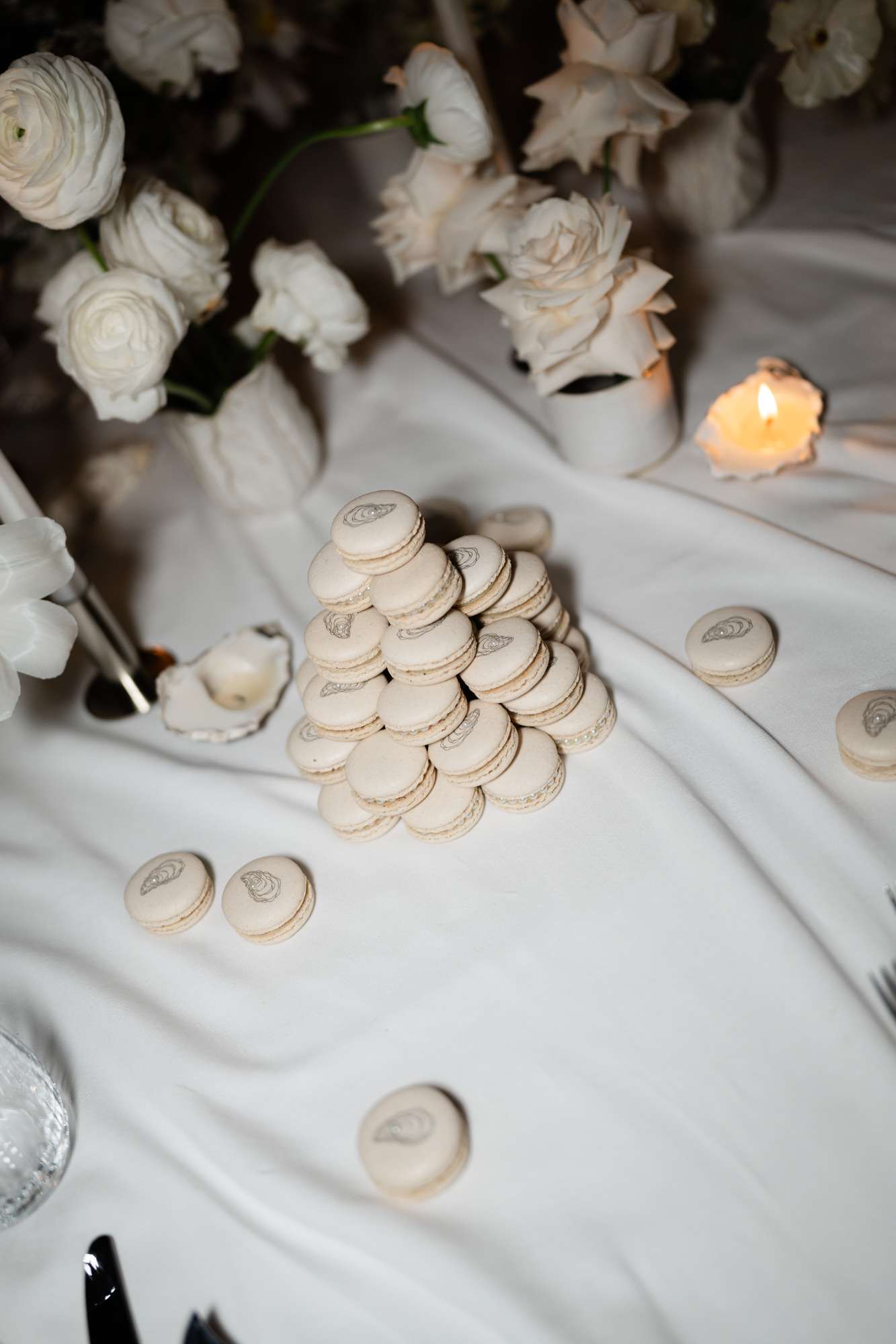 Gold-leaf macarons in pyramid formation surrounded by ivory roses, ranunculus, and lit pillar candle