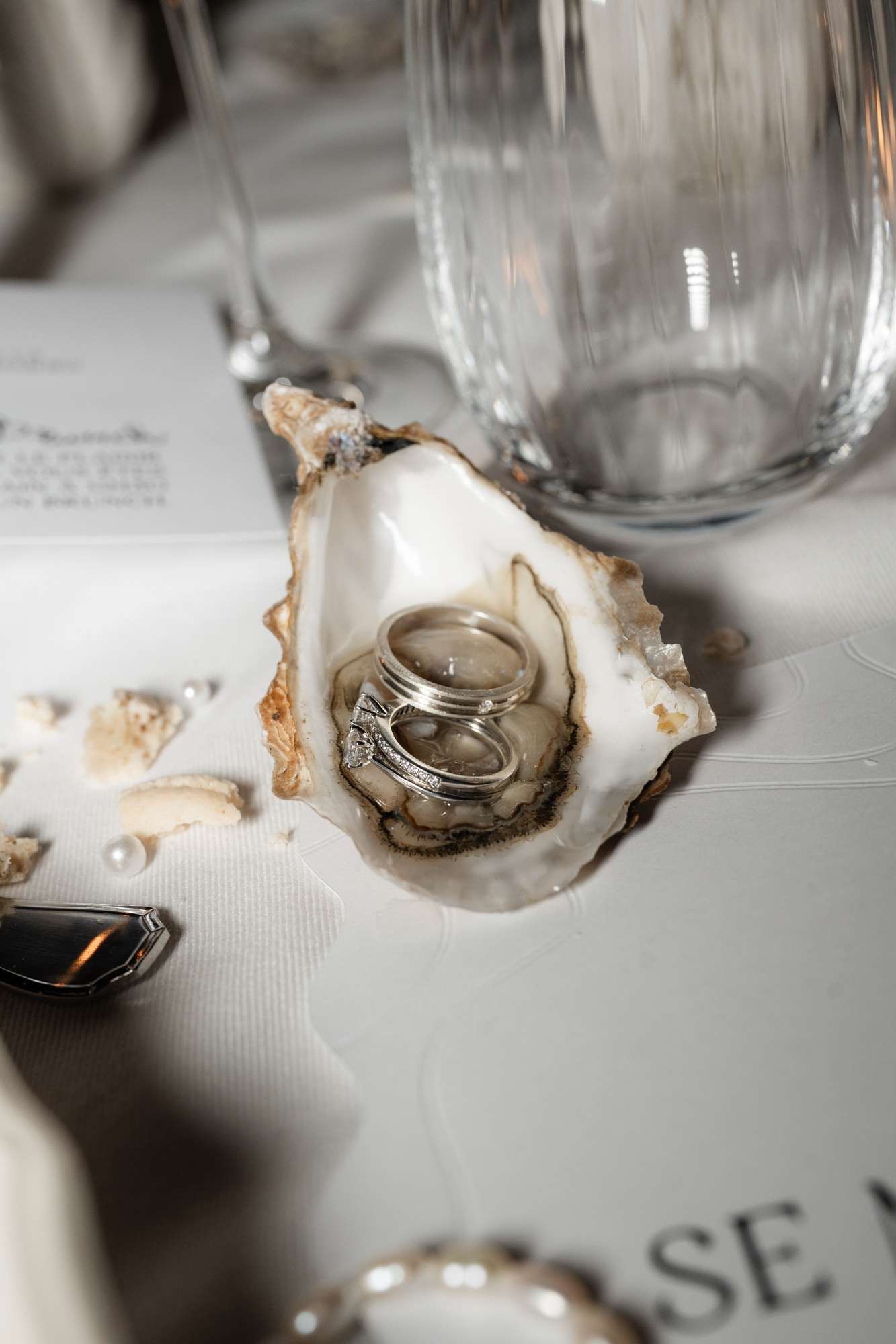 Wedding rings displayed inside an oyster shell on white textured placemat