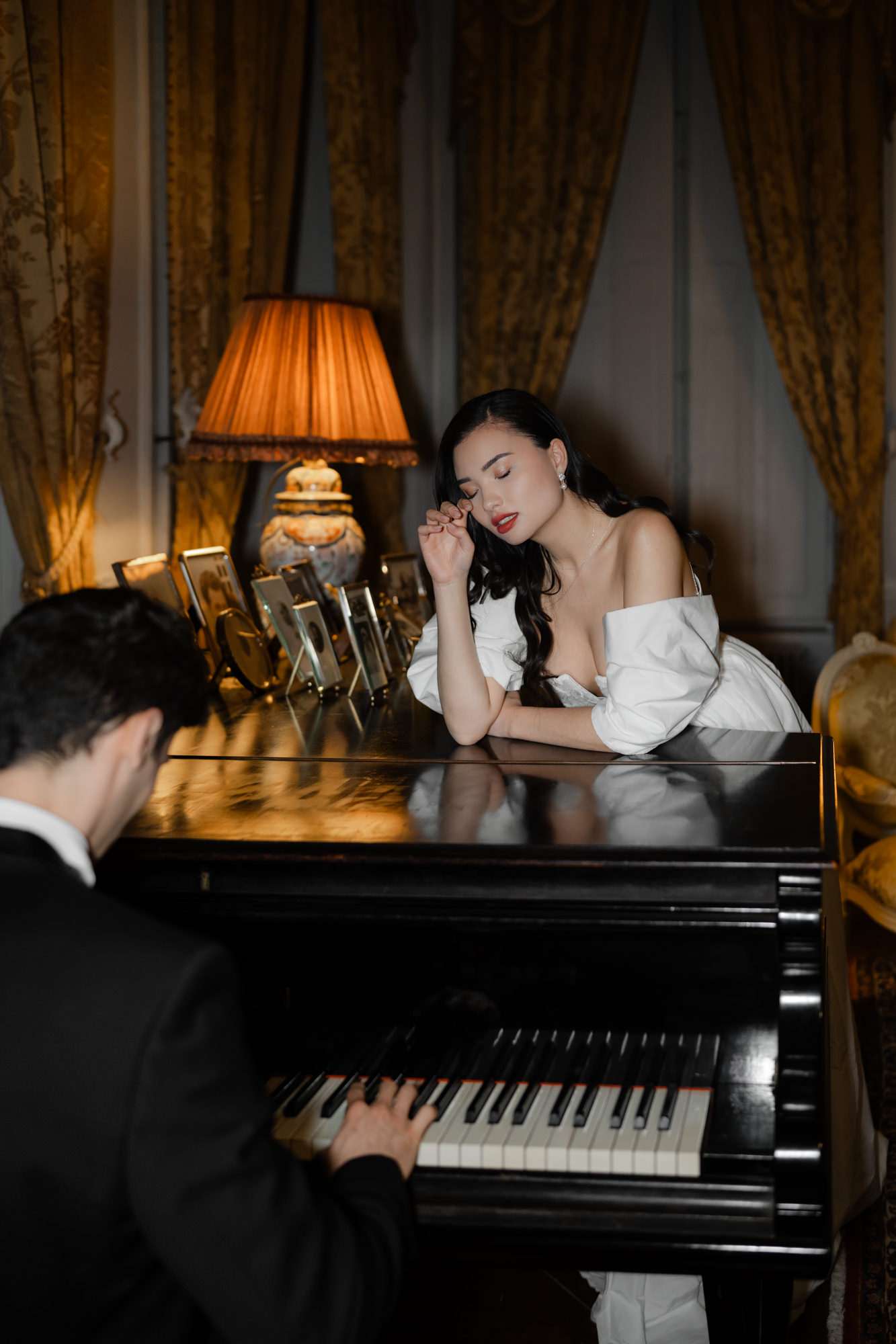 Bride and groom at black grand piano in amber-lit room with gold curtains