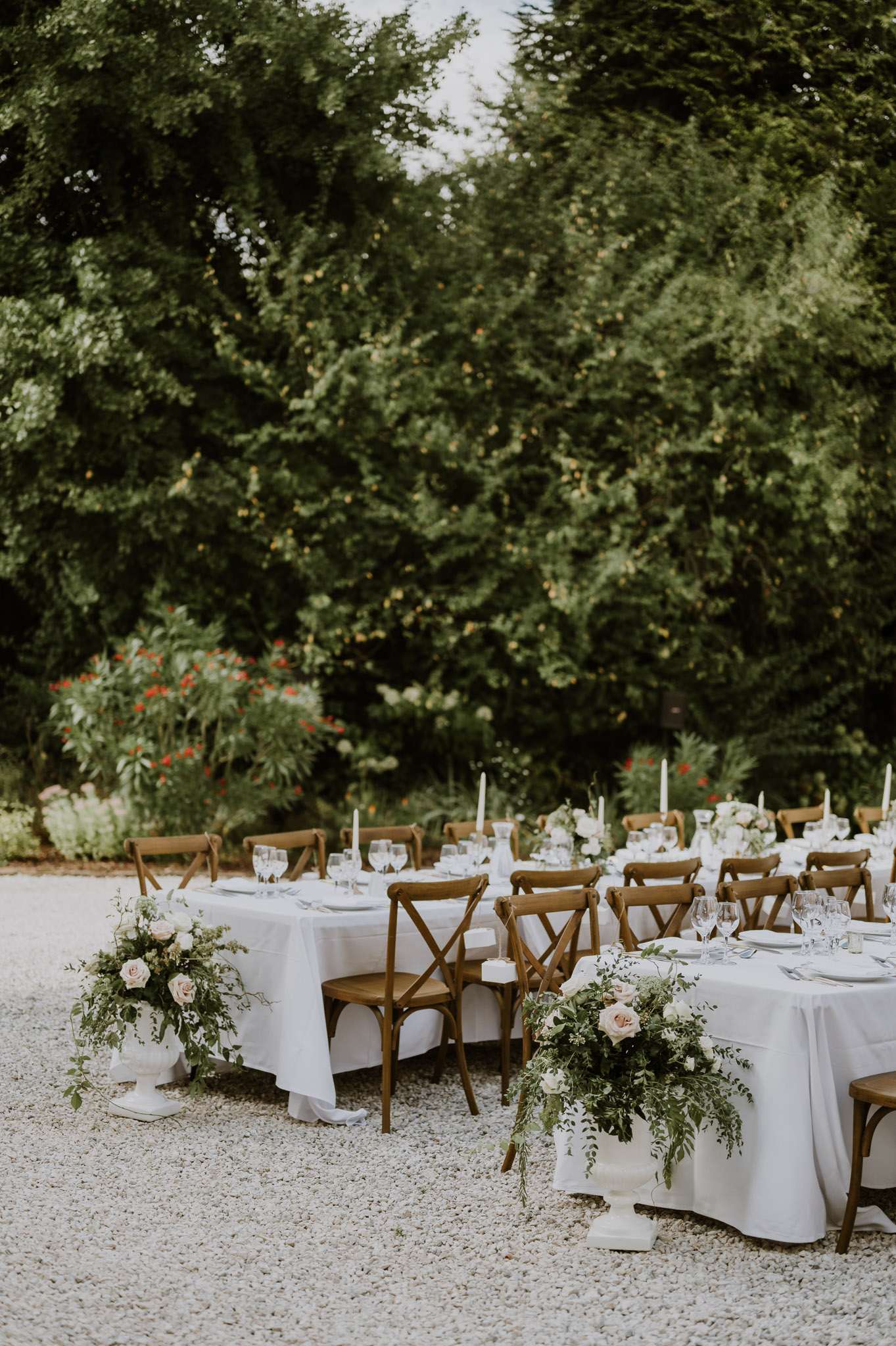 Long reception tables with white linens, cross-back chairs, and blush rose arrangements in white urns