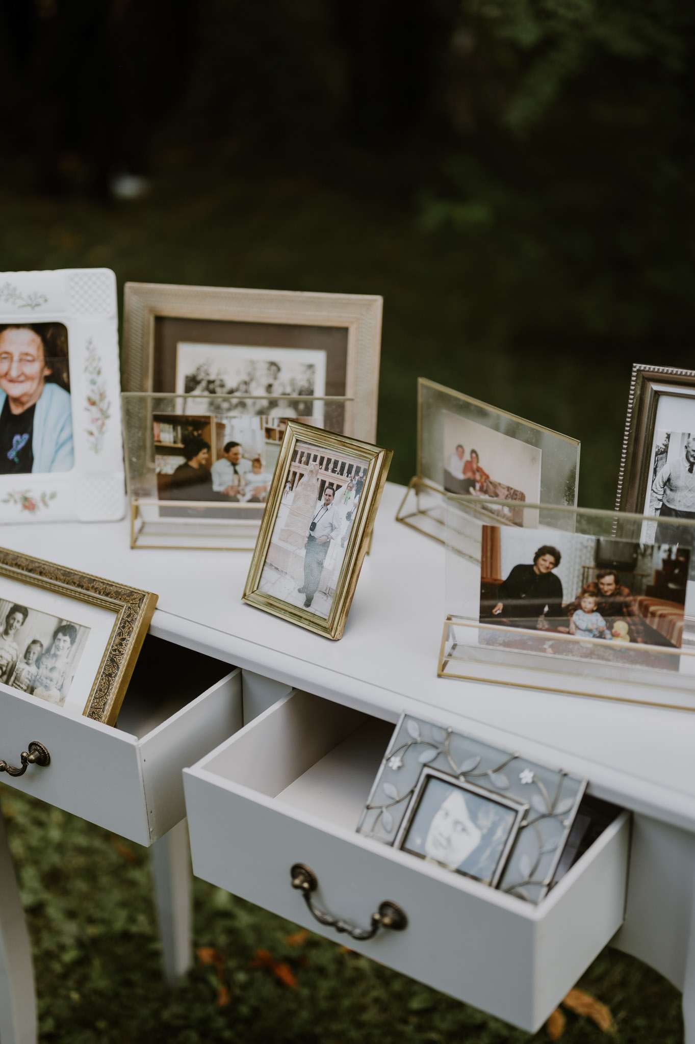 Memorial photo display on vintage white desk with framed family photographs in mixed frames