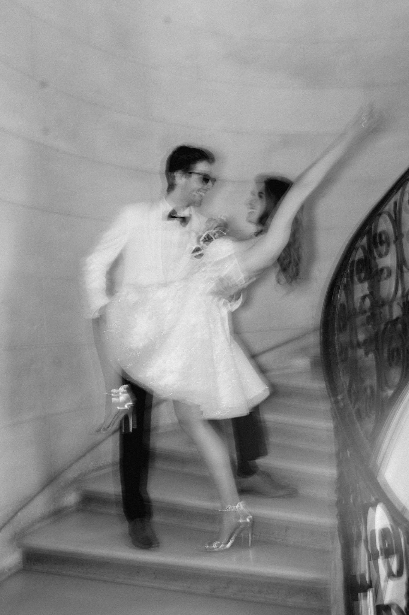 Black and white motion-blurred couple on wrought-iron staircase, bride in short mini dress with stilettos