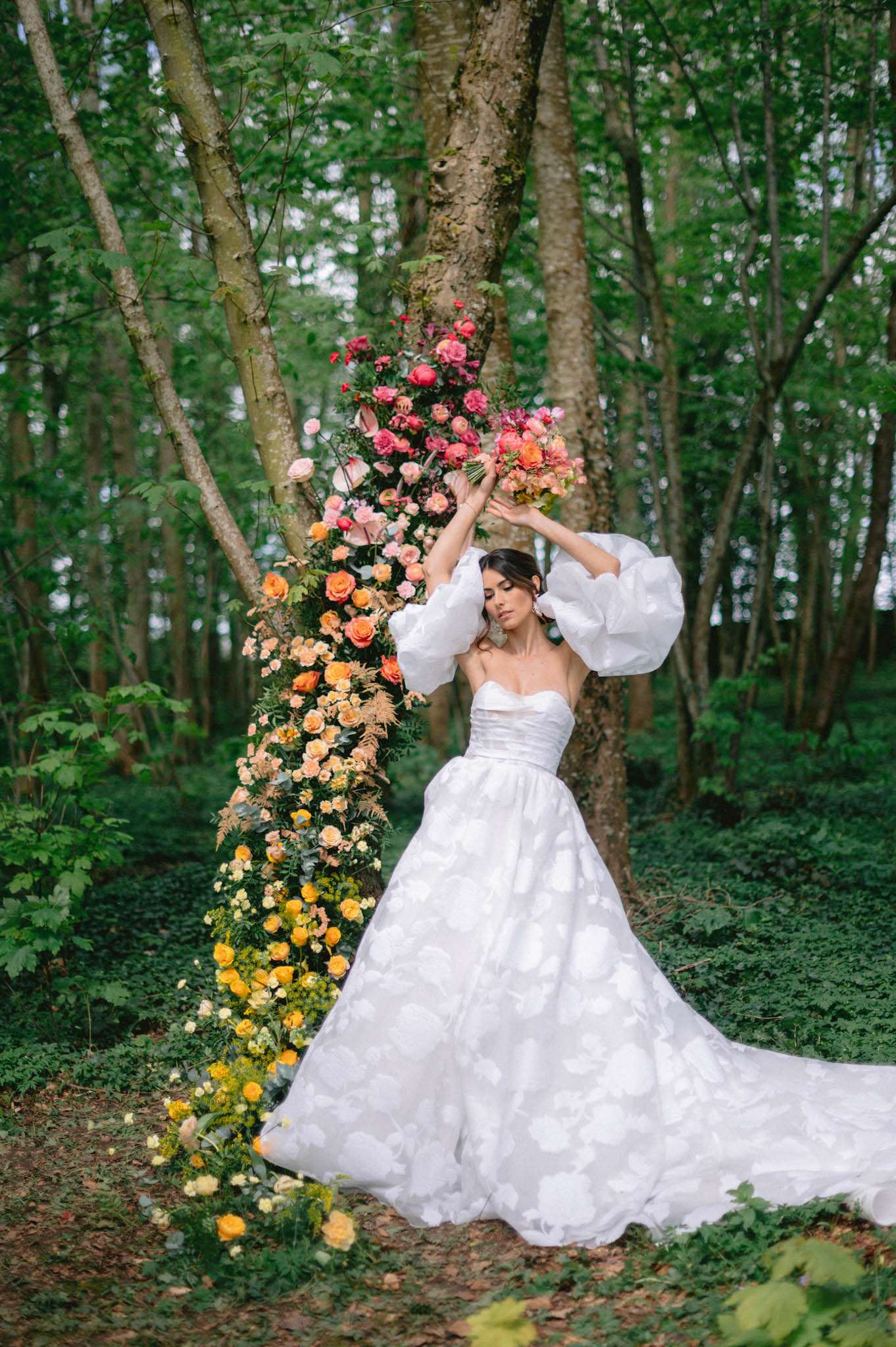 Bride in jacquard ballgown with puff sleeves holding pink bouquet beside ombre floral tree installation