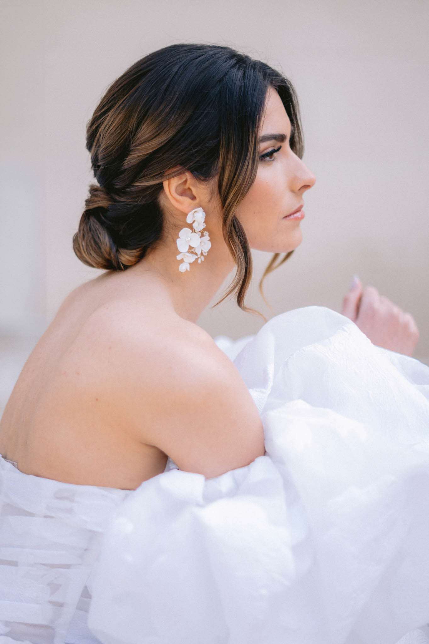 Three-quarter rear portrait of bride in strapless white gown with low chignon and white floral drop earrings