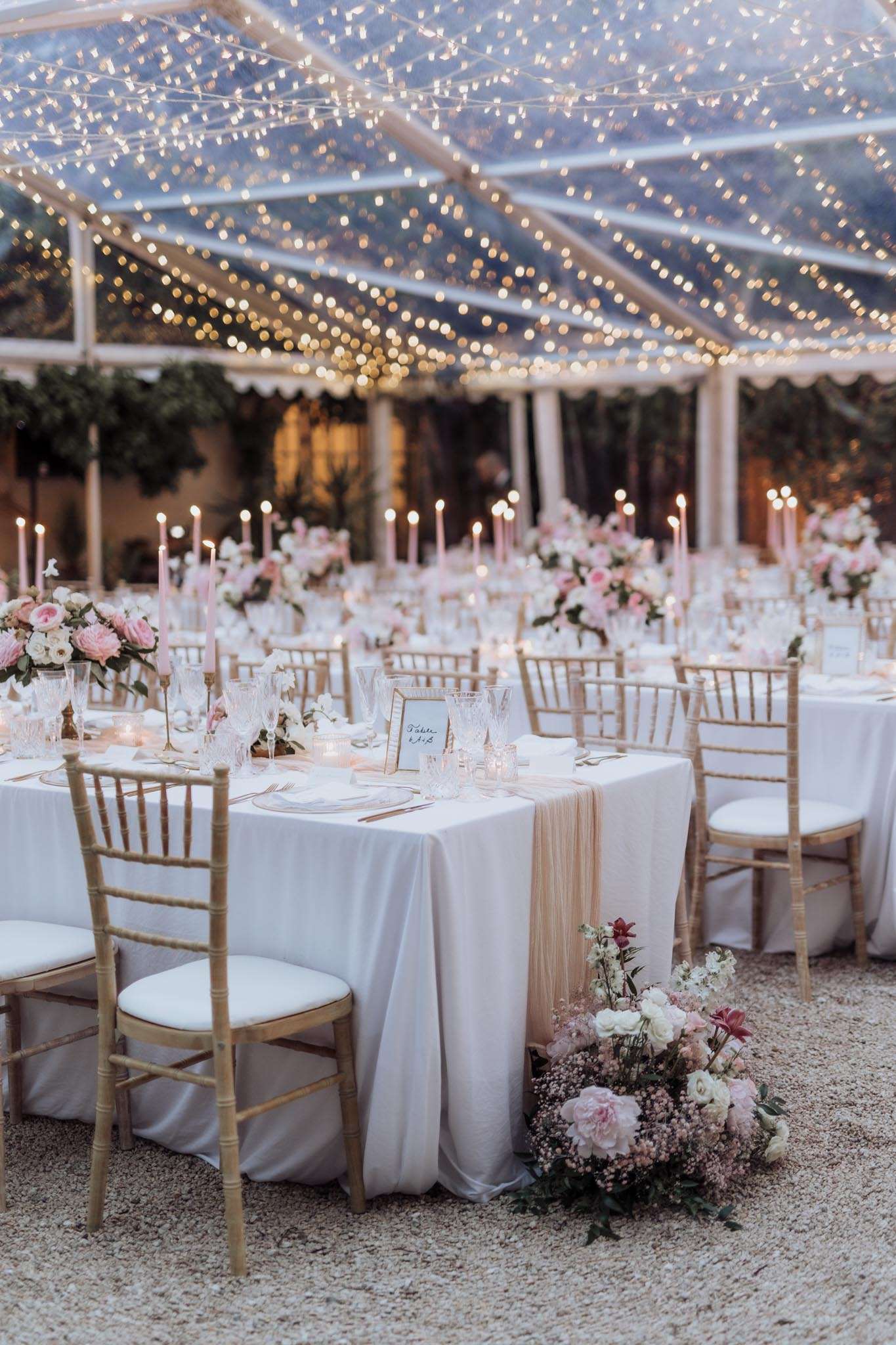 Reception under clear marquee with fairy lights, round tables with blush roses, gold chiavari chairs