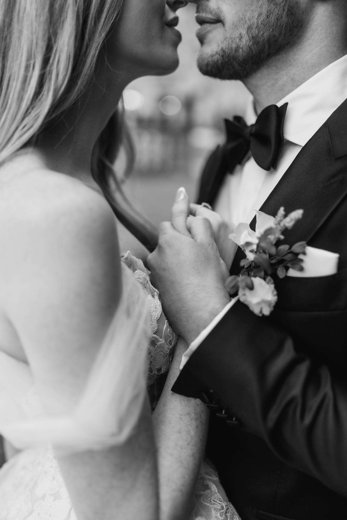 Black-and-white close-up of bride and groom about to kiss showing lace dress detail and boutonniere