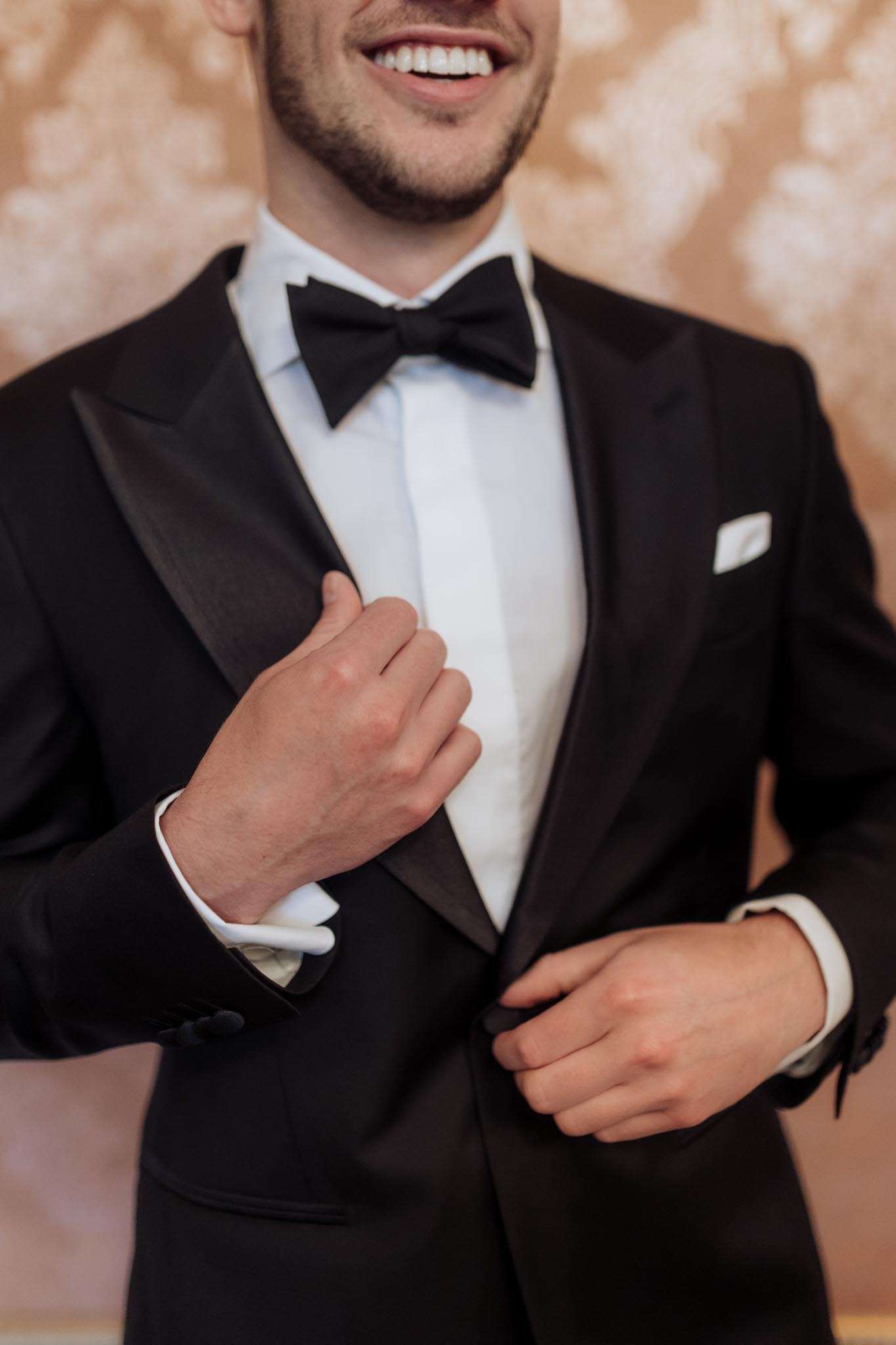 Groom adjusting black tuxedo jacket with satin lapels bow tie and white pocket square