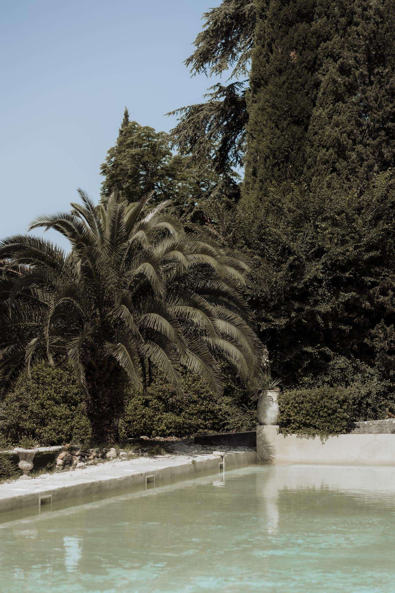Turquoise ornamental pool with stone surround and terracotta urn in lush garden setting