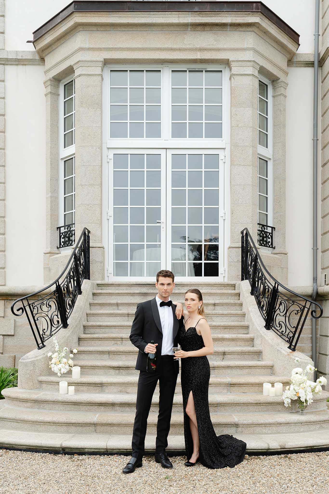 Couple on grand stone steps beside white hydrangea planters and pillar candles at classical cream stone faÃ§ade