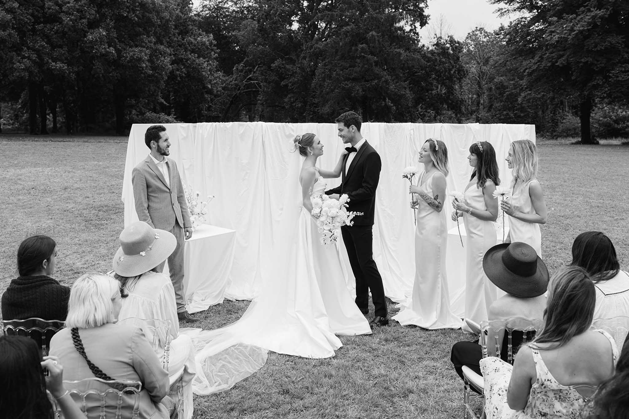 Black-and-white outdoor ceremony under white fabric backdrop with trees framing the scene