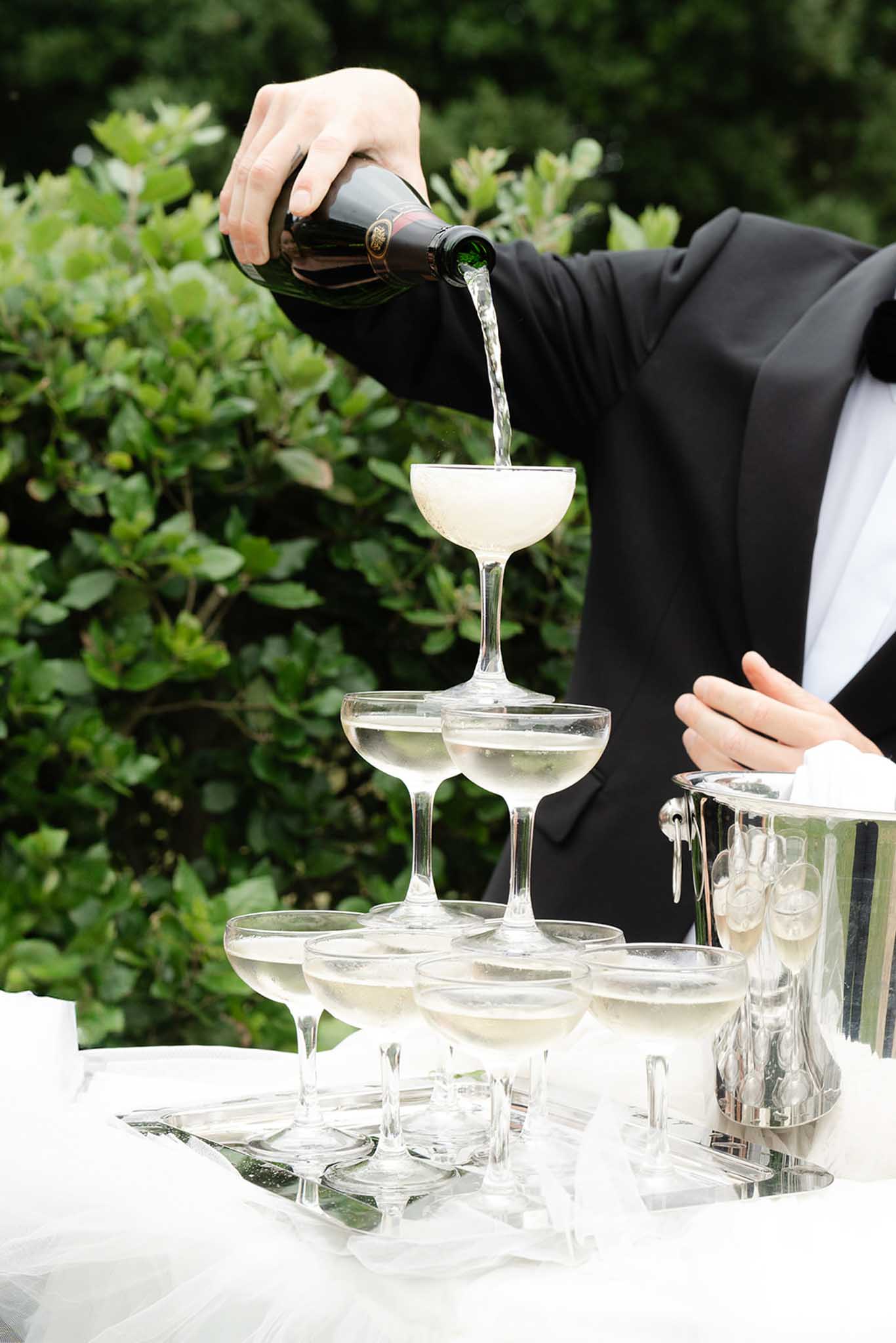 Champagne being poured into a coupe glass tower during an outdoor garden wedding reception
