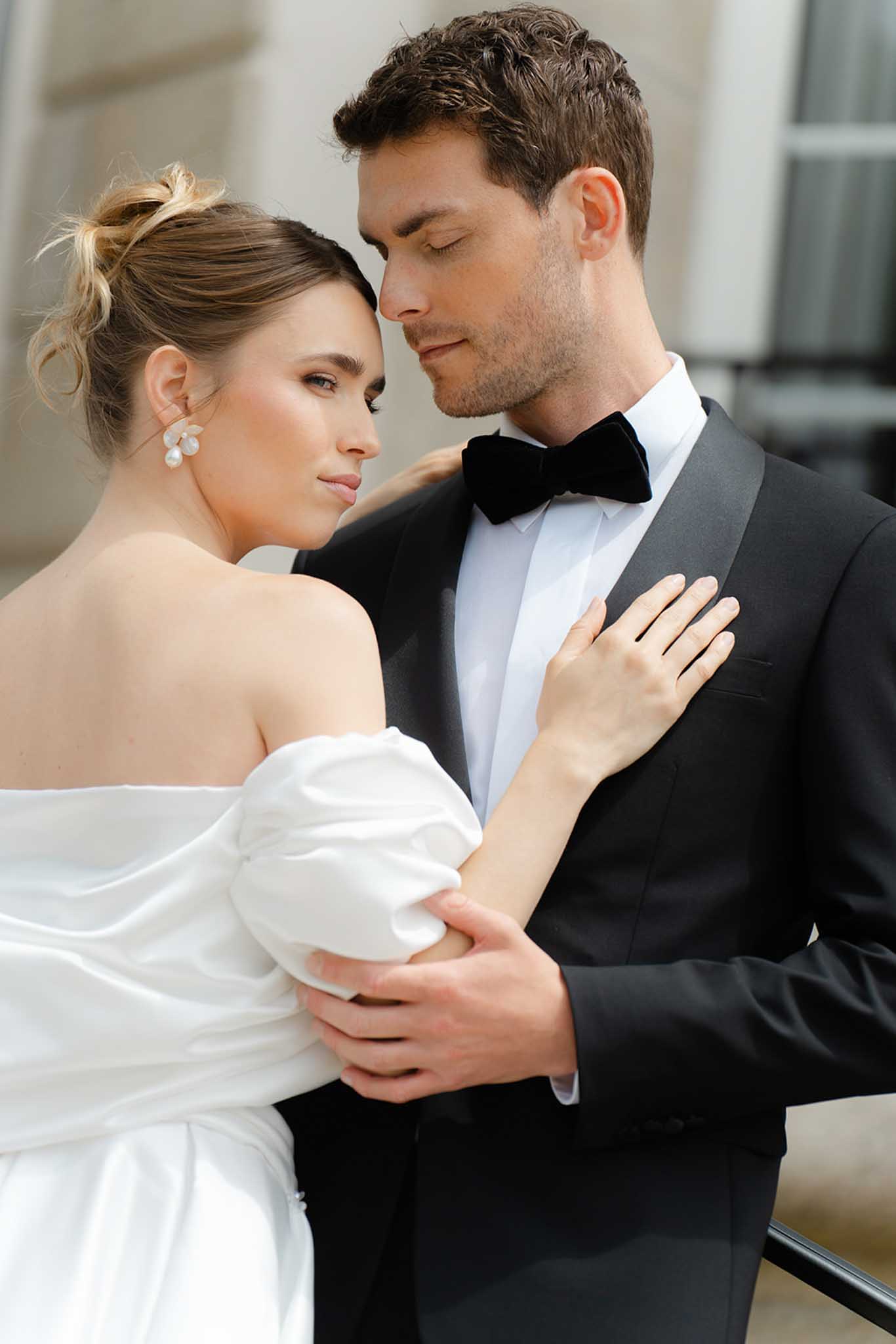 Close-up profile portrait of bride in strapless ivory dress and groom in charcoal suit sharing an intimate moment indoors