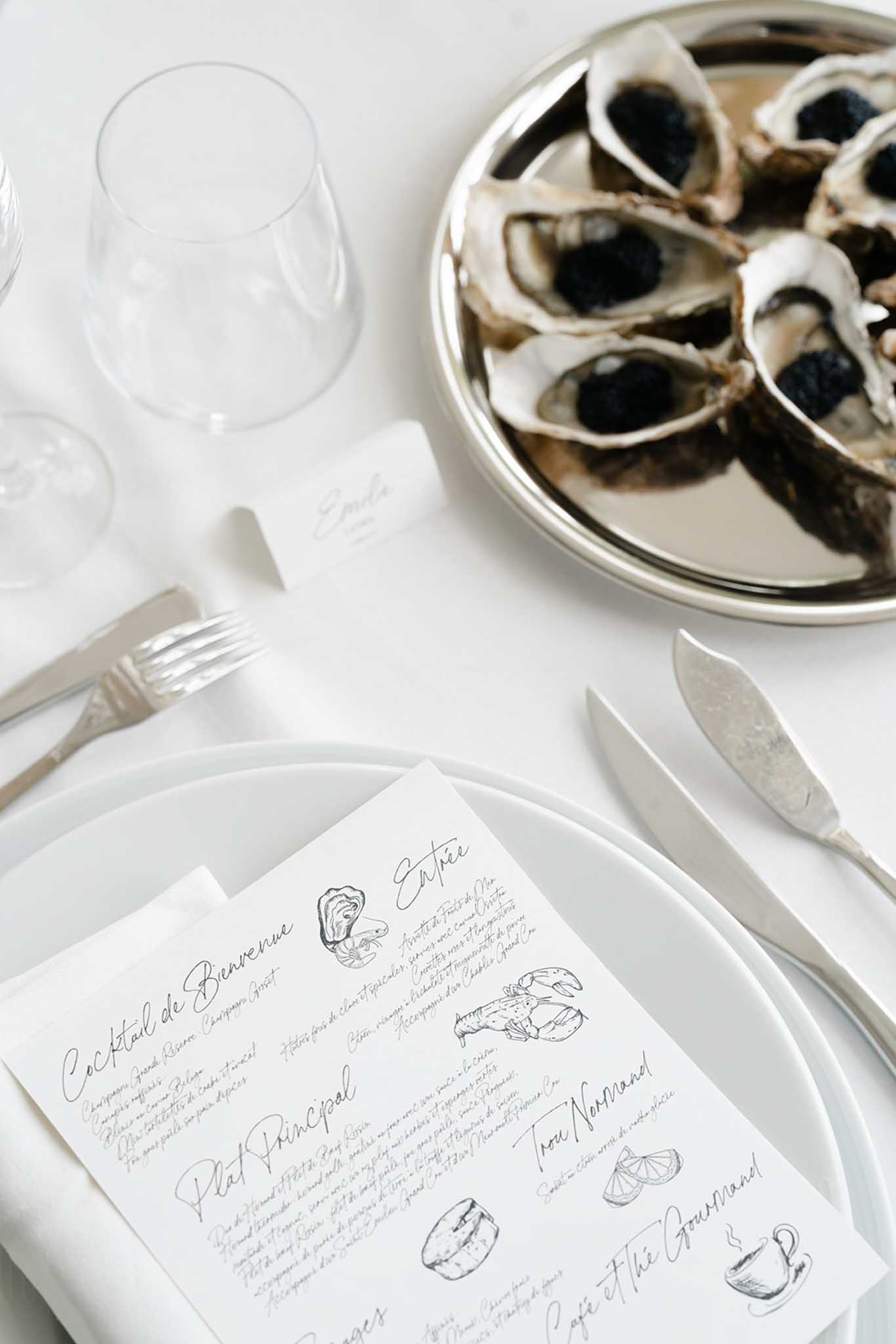Wedding place setting flat lay with handwritten seafood menu card, silver flatware, and oysters on ice