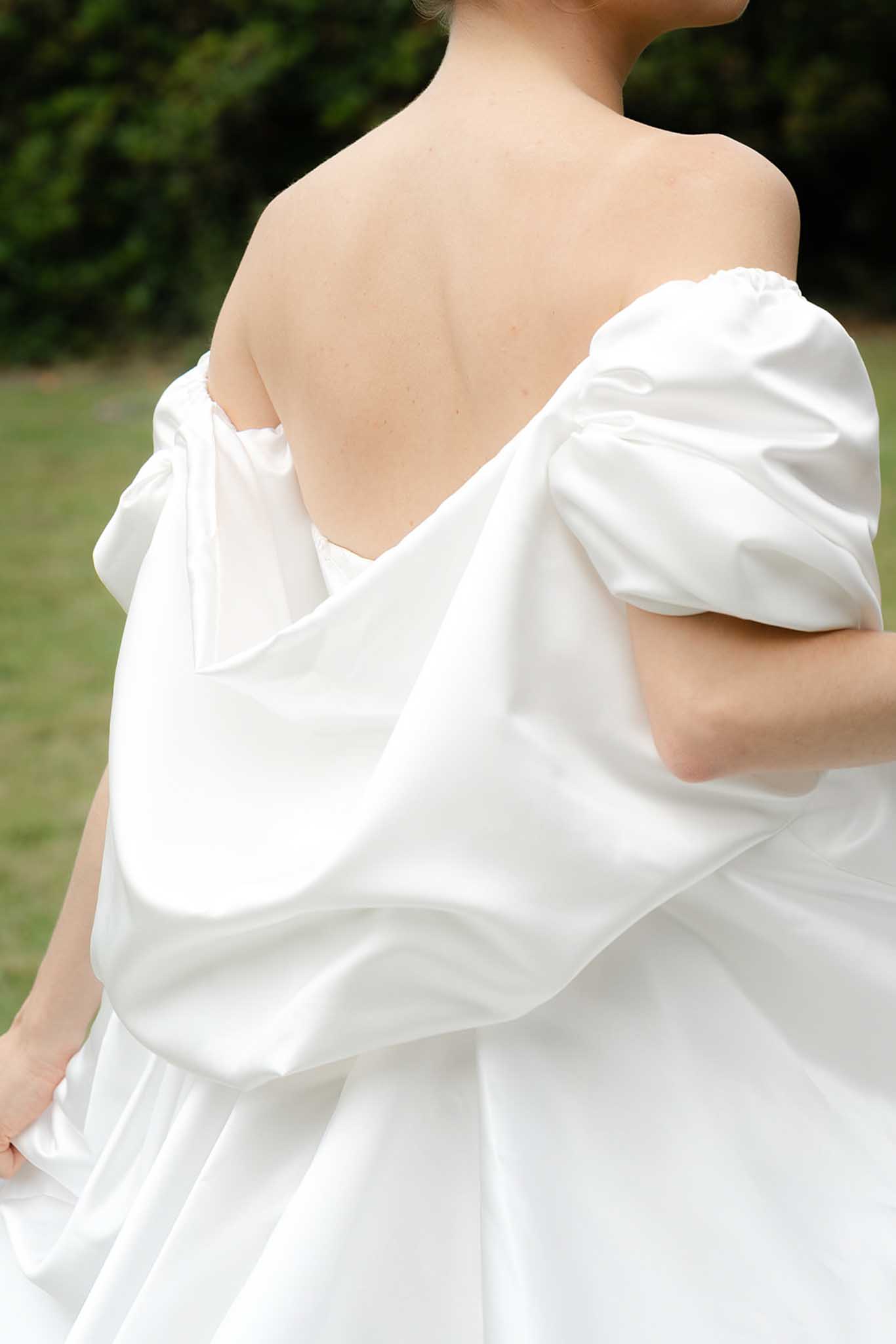 Close-up of bride's back showing ivory gown with low V-back neckline and romantic puffed off-shoulder sleeves