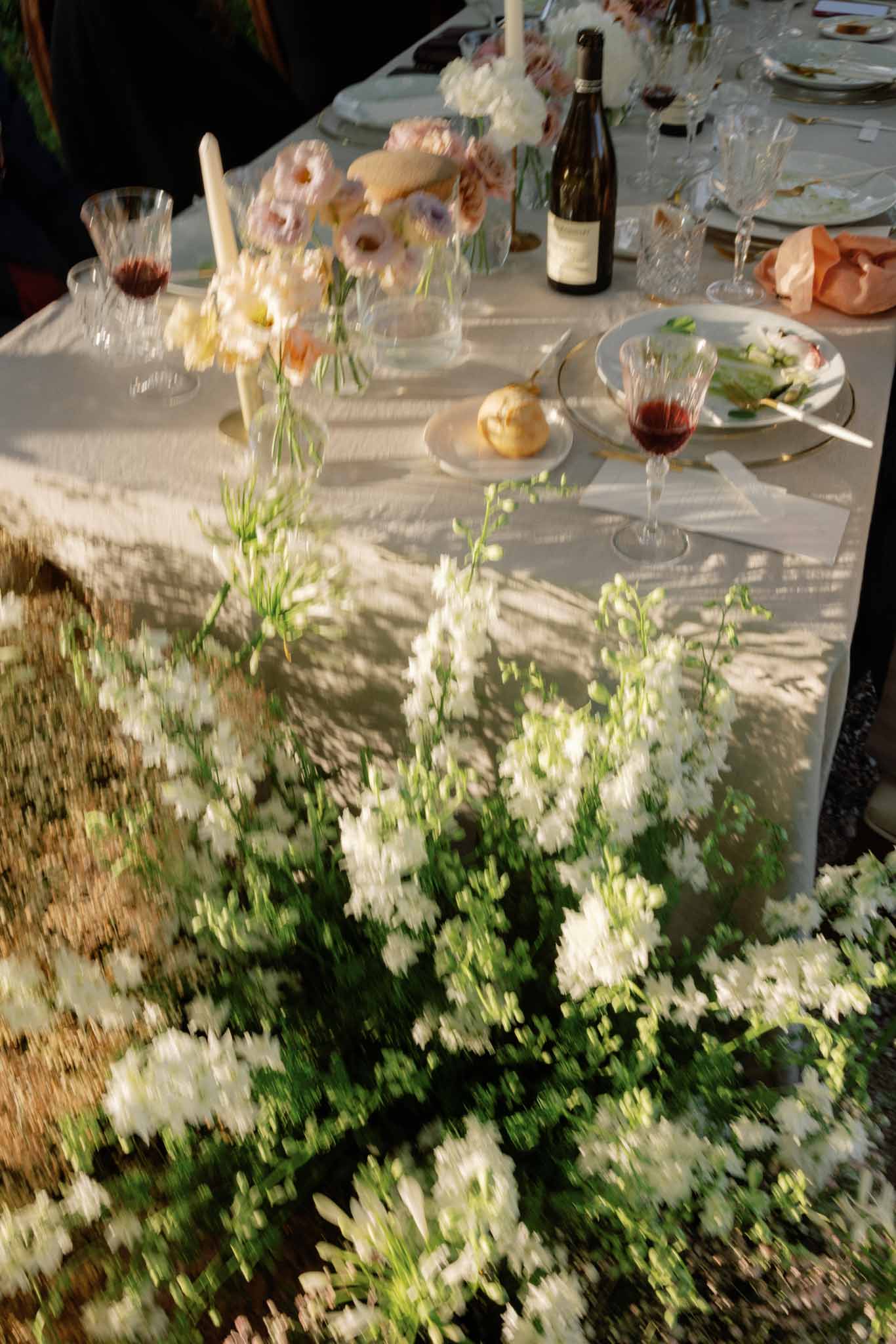 Outdoor reception table with floral runner of white and pink flowers, clear vases, and place settings