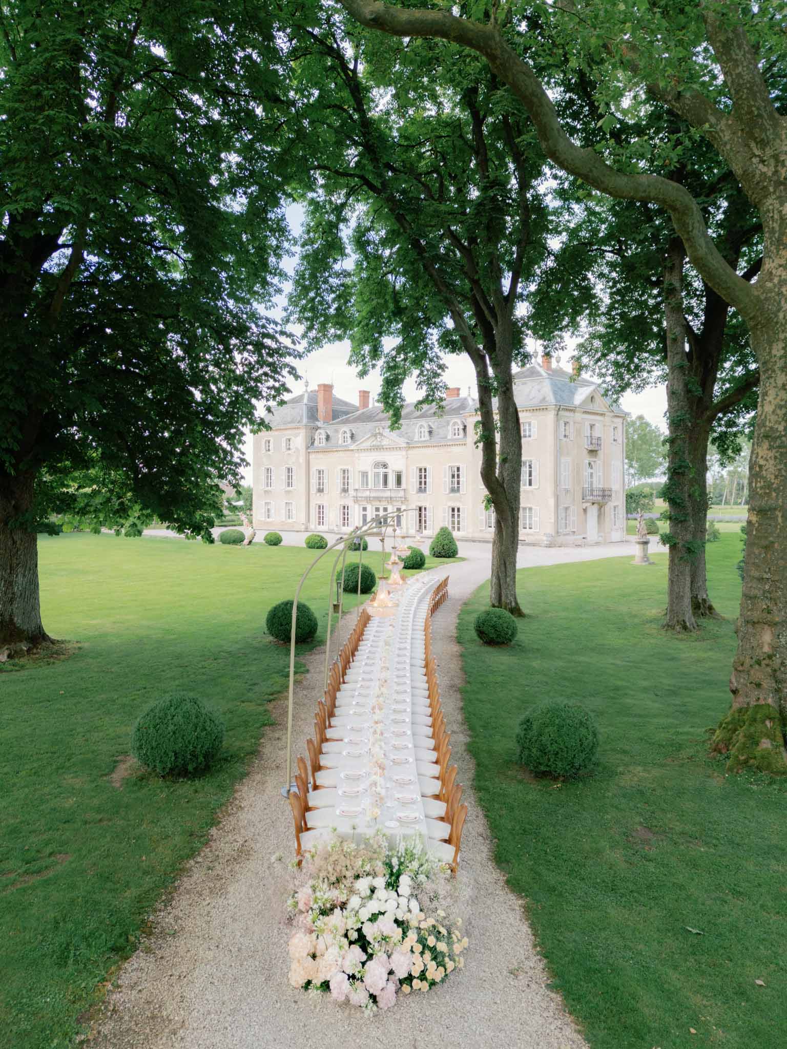Gravel ceremony aisle lined with folding chairs leading to Chateau de Varennes with floral arrangement
