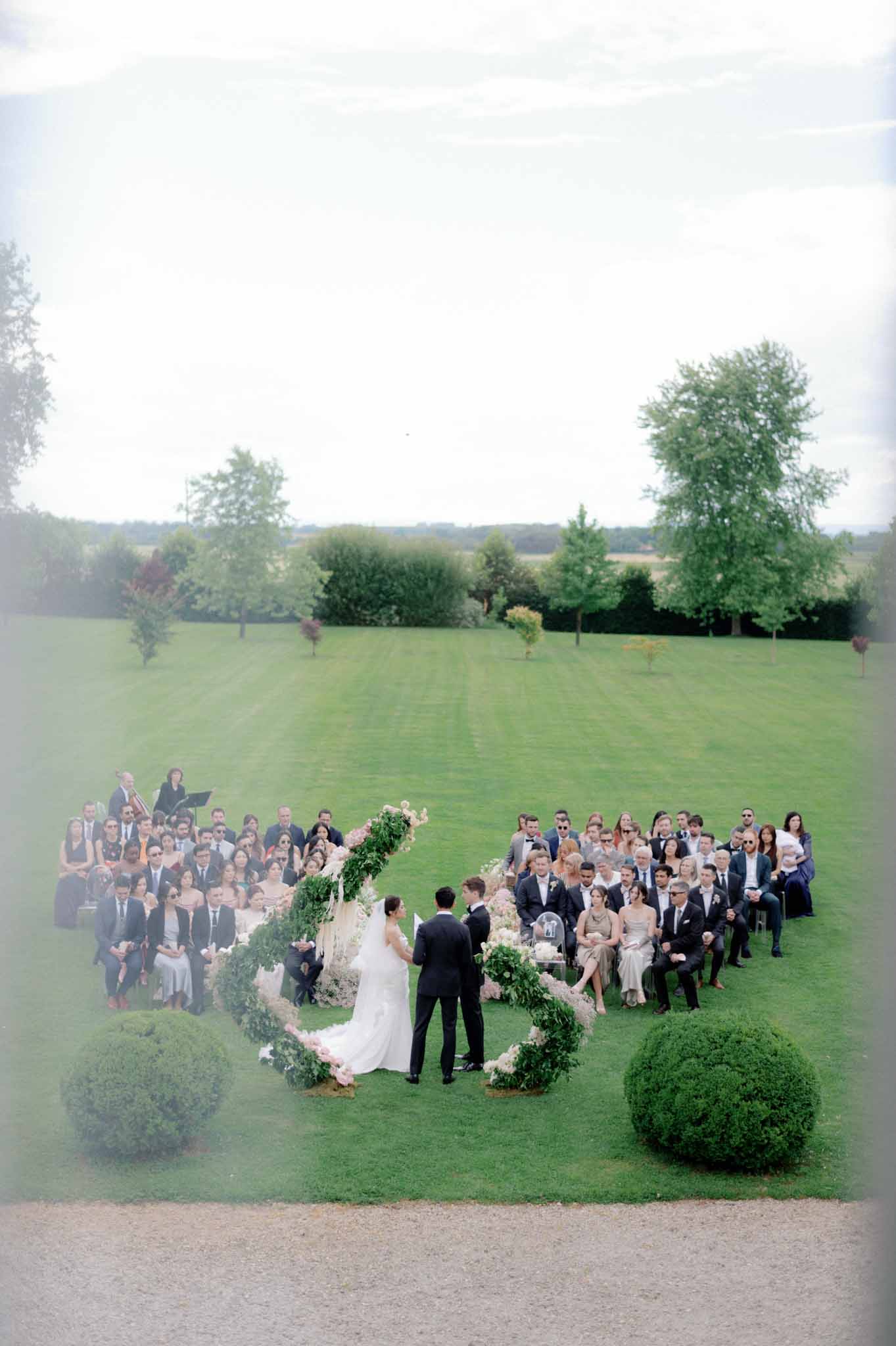 Aerial view of outdoor ceremony with bride and groom in circular greenery frame and sixty seated guests