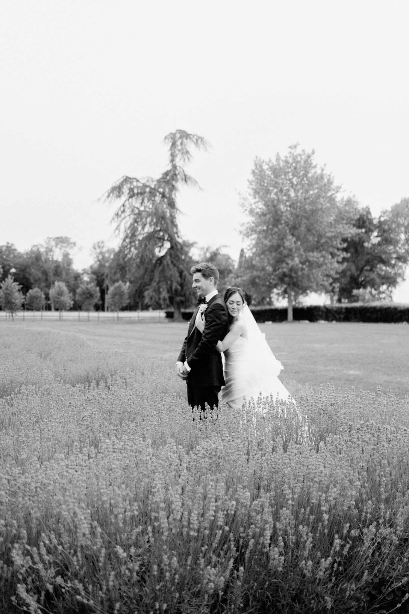Black-and-white couple in formal attire walking through estate grounds with weeping trees in background